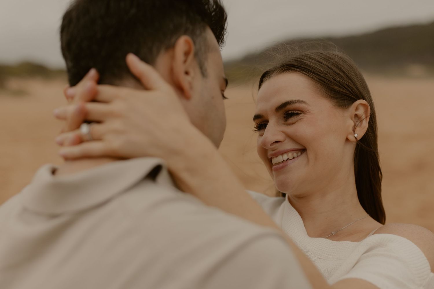 A couple shares an intimate moment together on a beach at sunset with warm golden lighting.