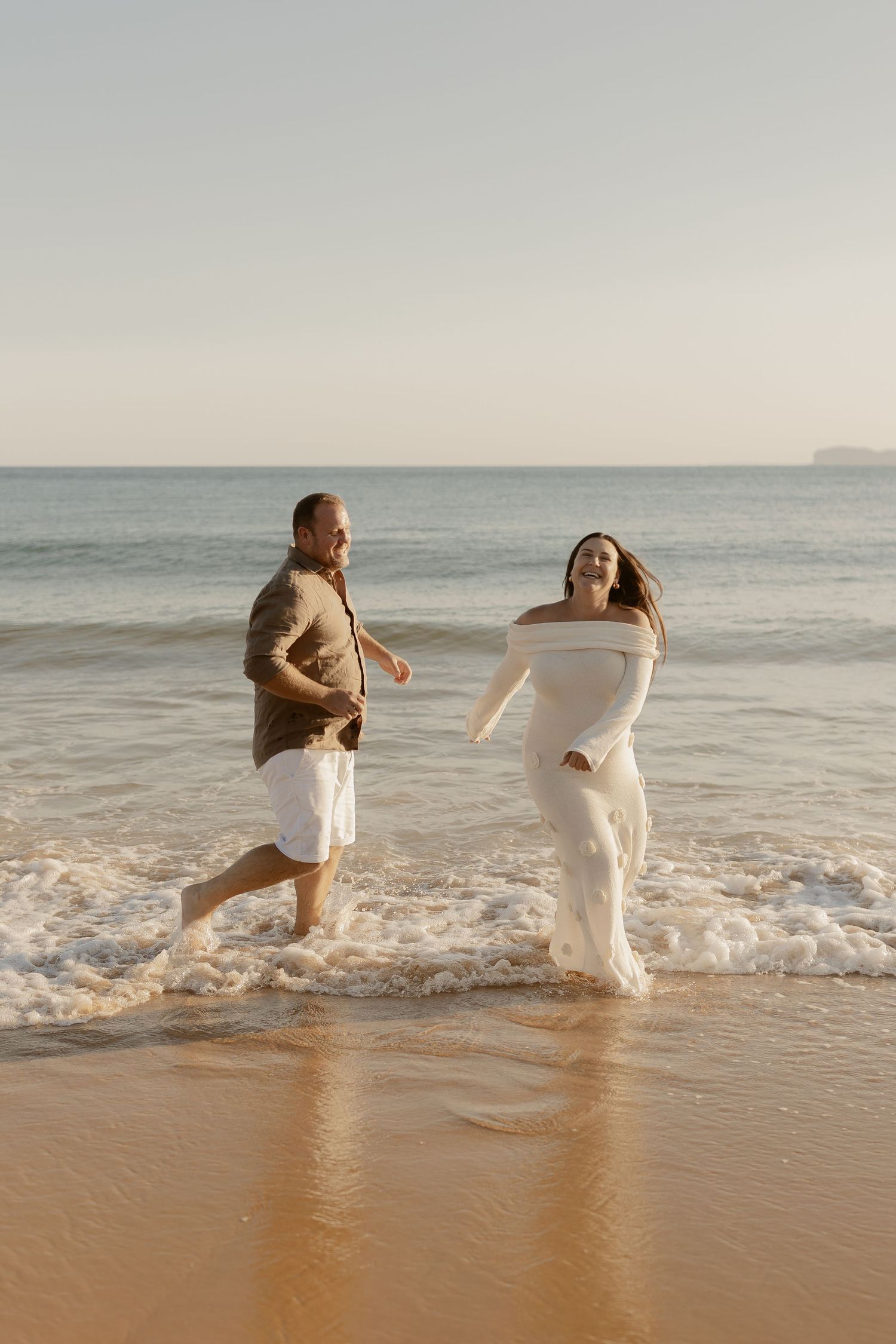 People splashing and playing in ocean waves at sunset on a beach.