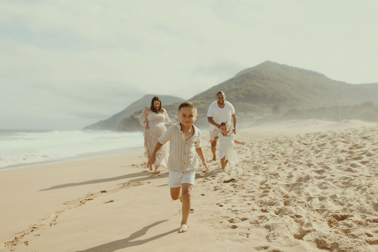 People walking and leaving footprints on a sandy beach with mountains in the background during a sunny day.