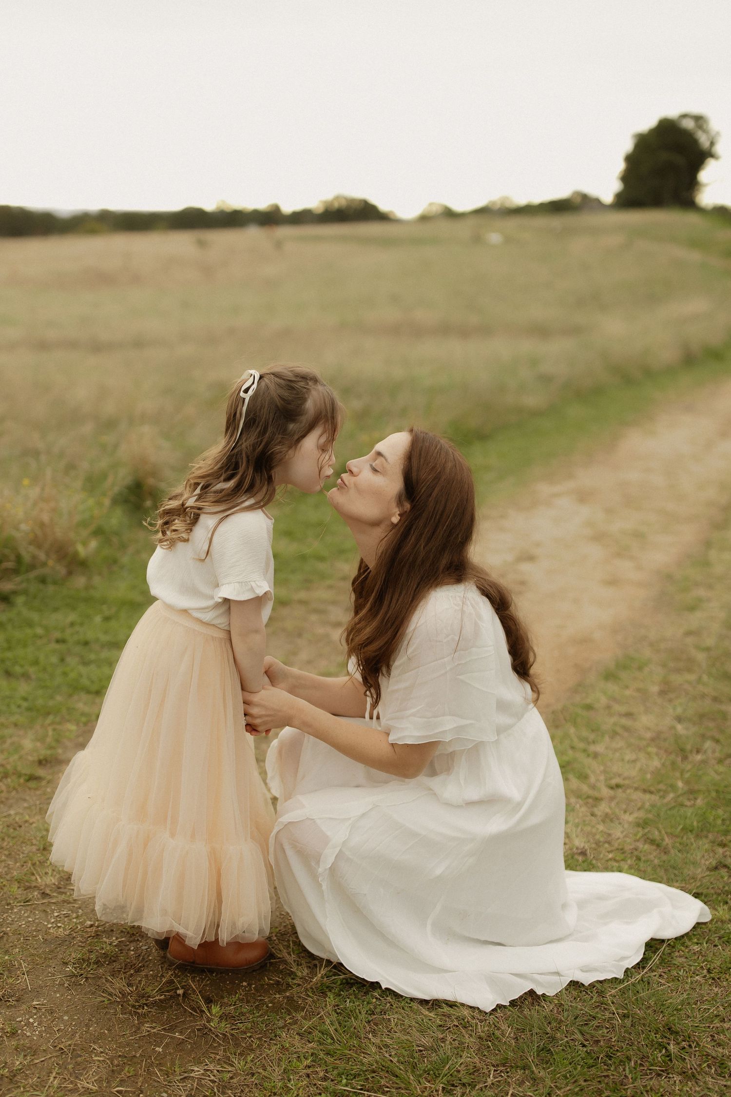 Tender moment between two people in matching white and cream outfits sitting on a grassy path at sunset.