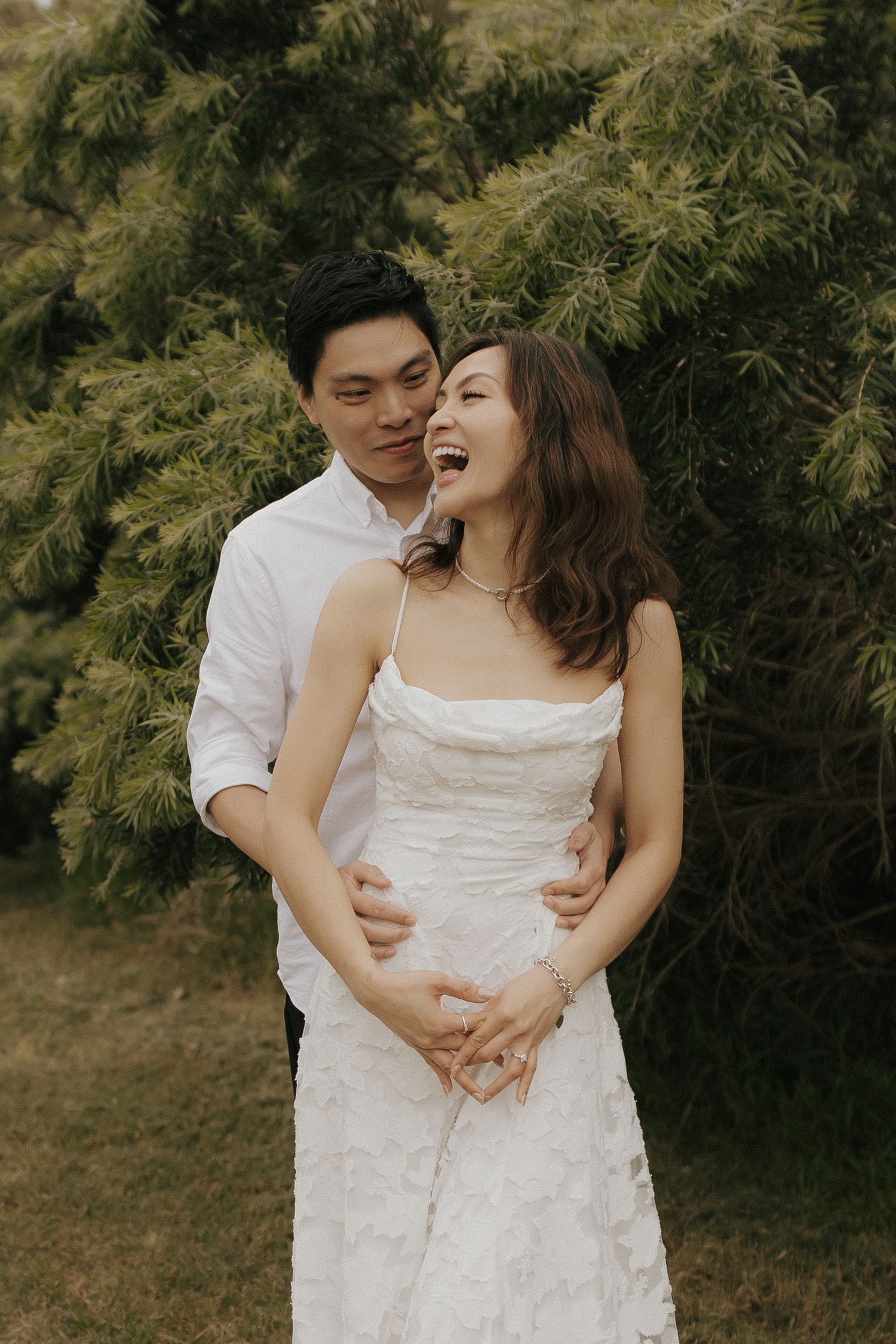 A couple in white clothing shares intimate candid moments while embracing in a garden setting.
