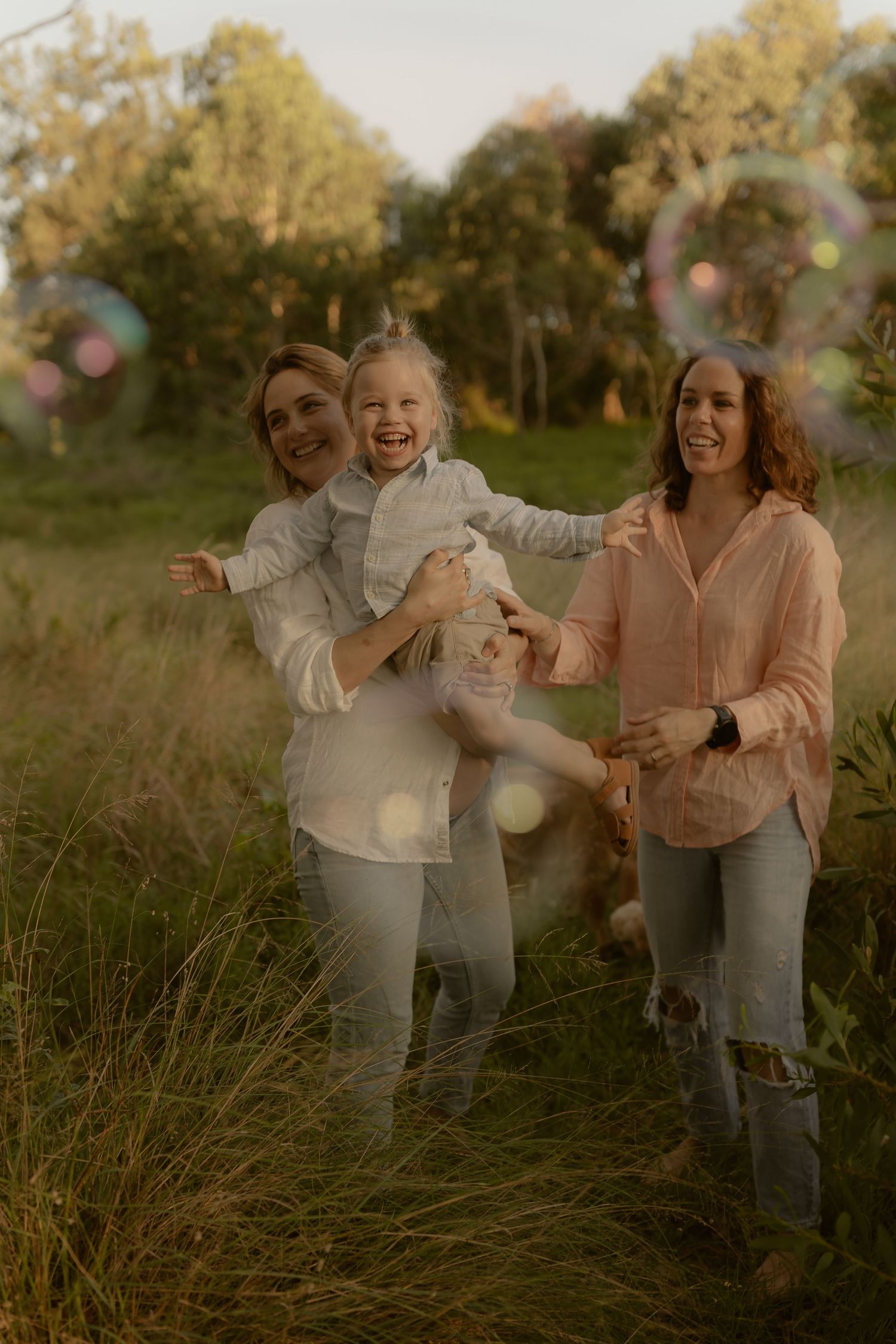 Family enjoying a playful moment together in a meadow during sunset with golden light and tall grass.