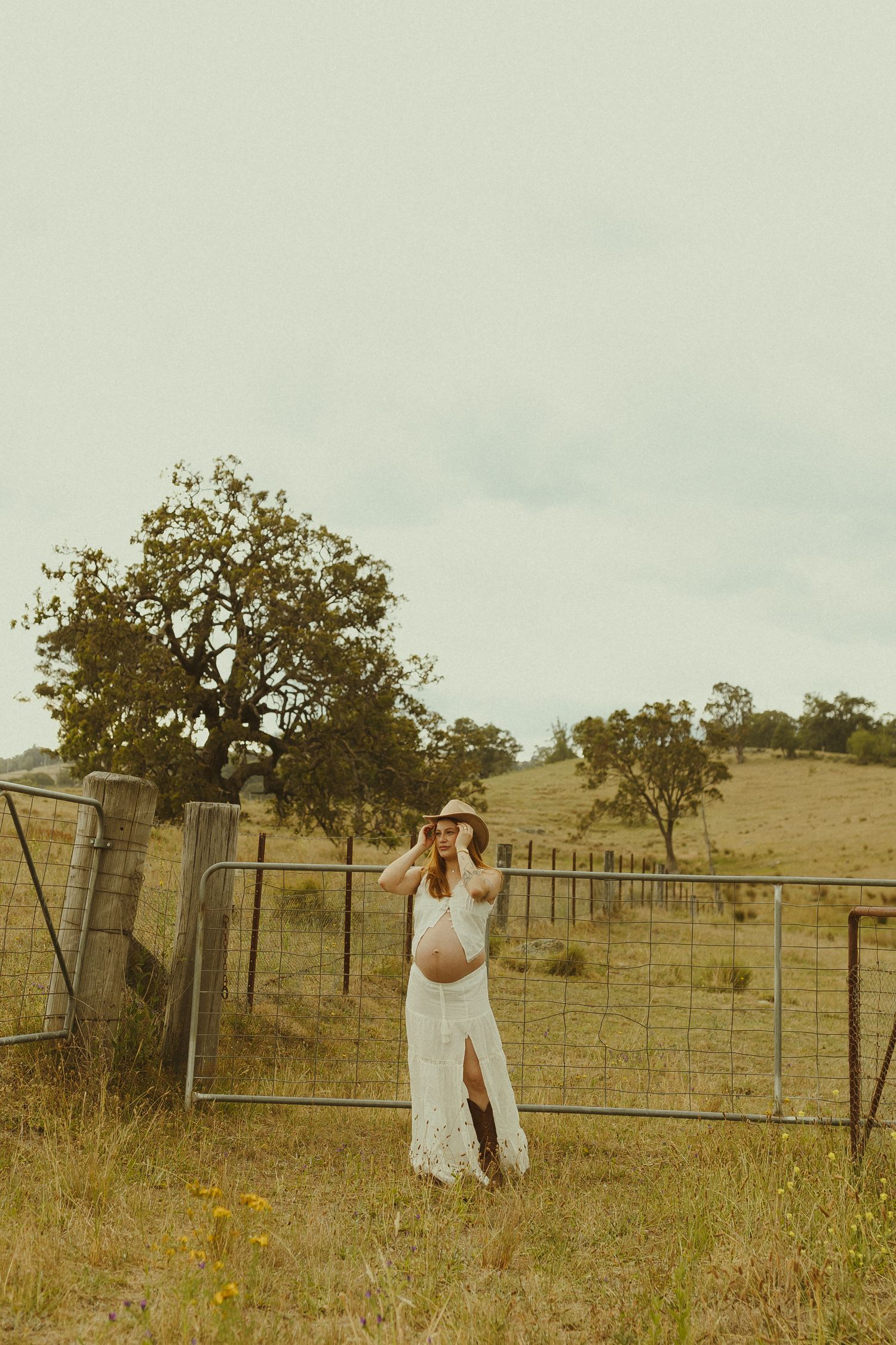 Ethereal countryside portrait session with flowing white dress and metal gate in golden afternoon light.