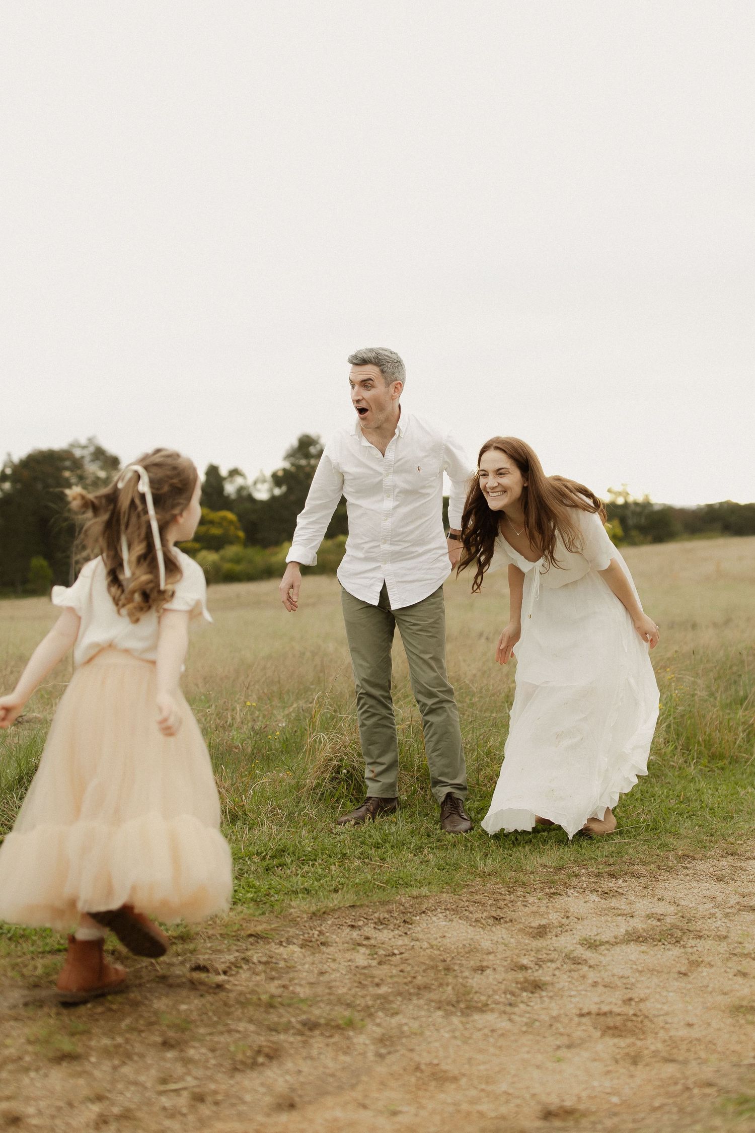 Family in white and cream outfits playing and running together in a grassy field at sunset.