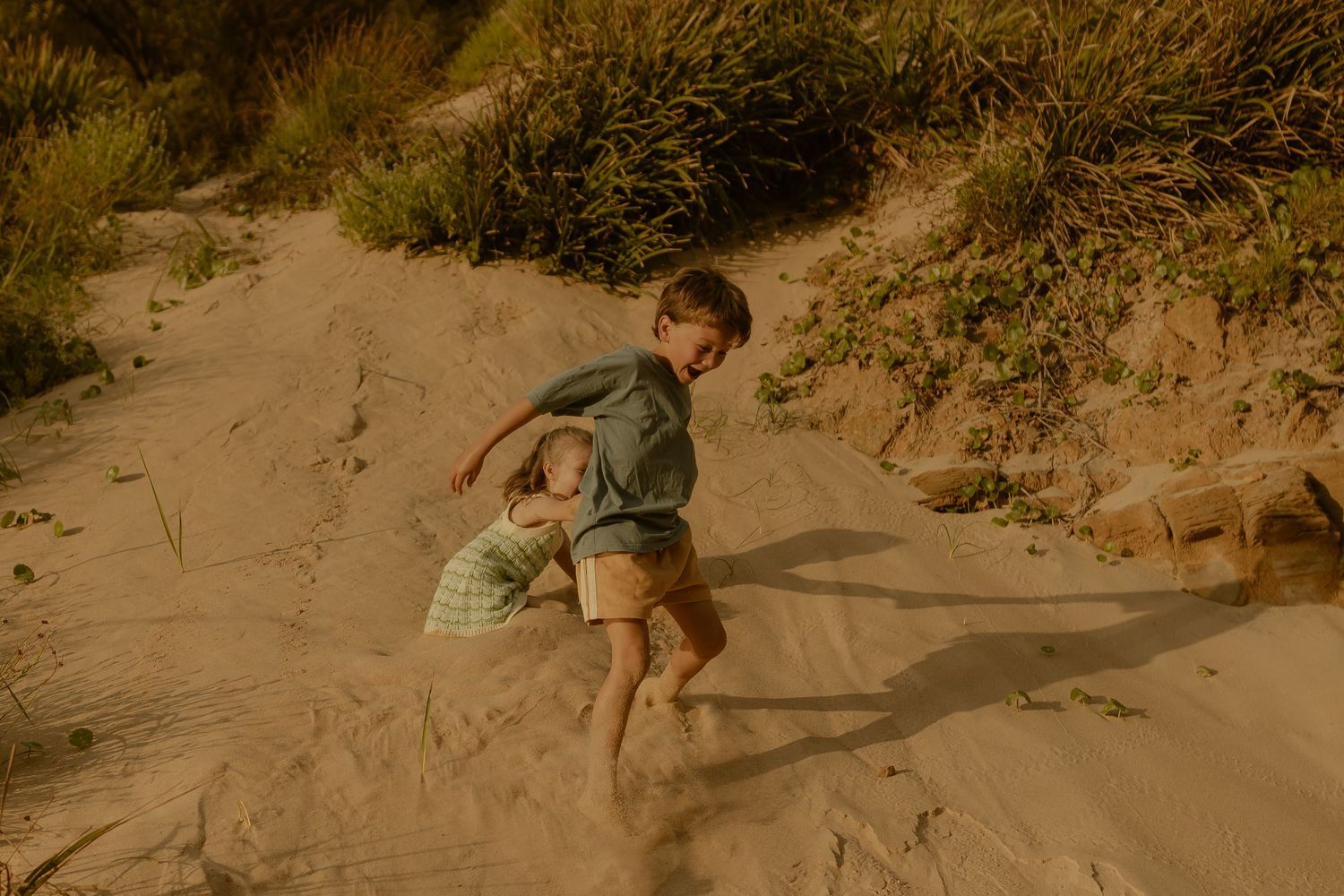 Children climb and play on sandy dunes covered with beach grass.