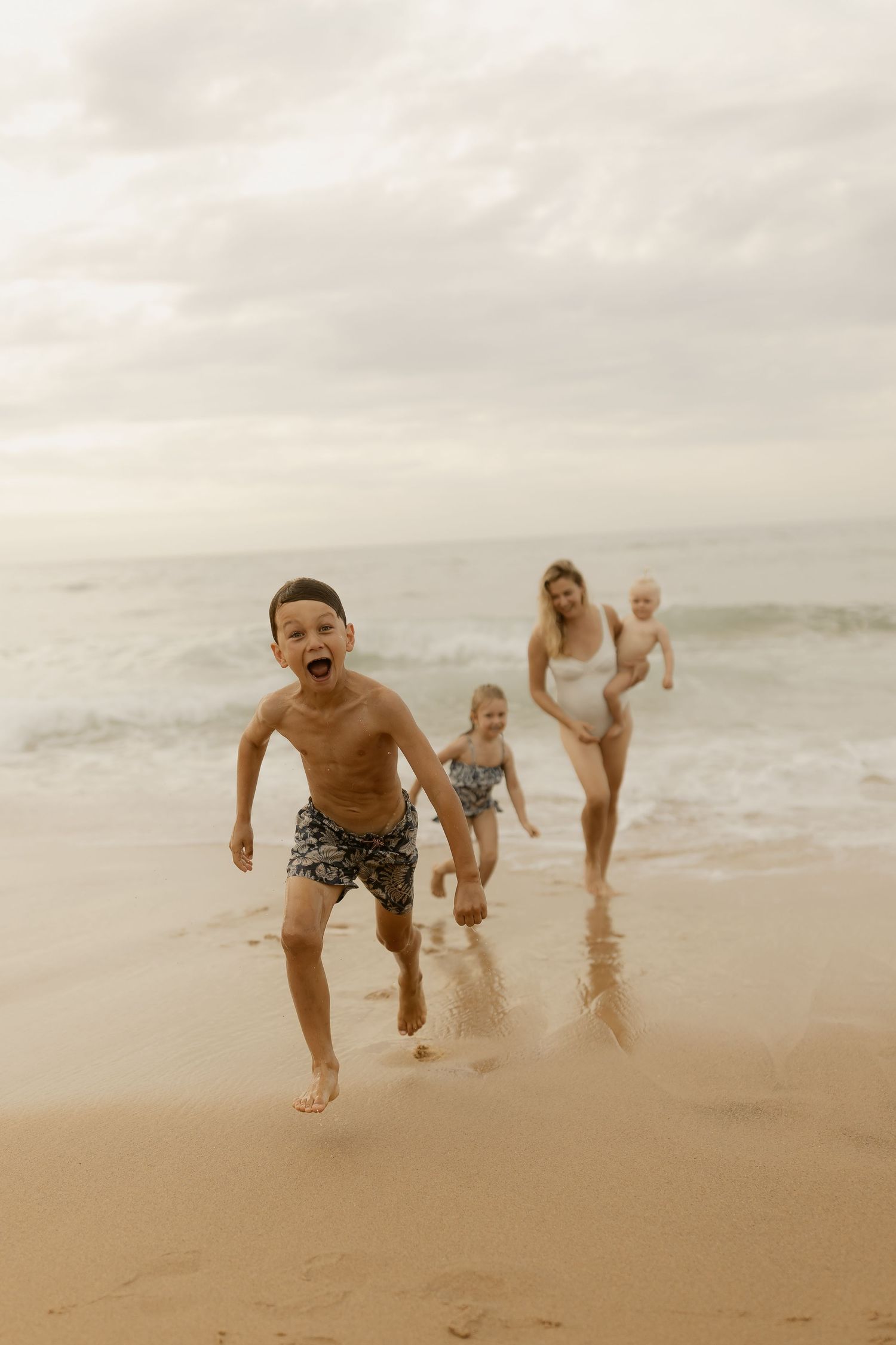 People run and play along a misty beach shoreline on an overcast day.