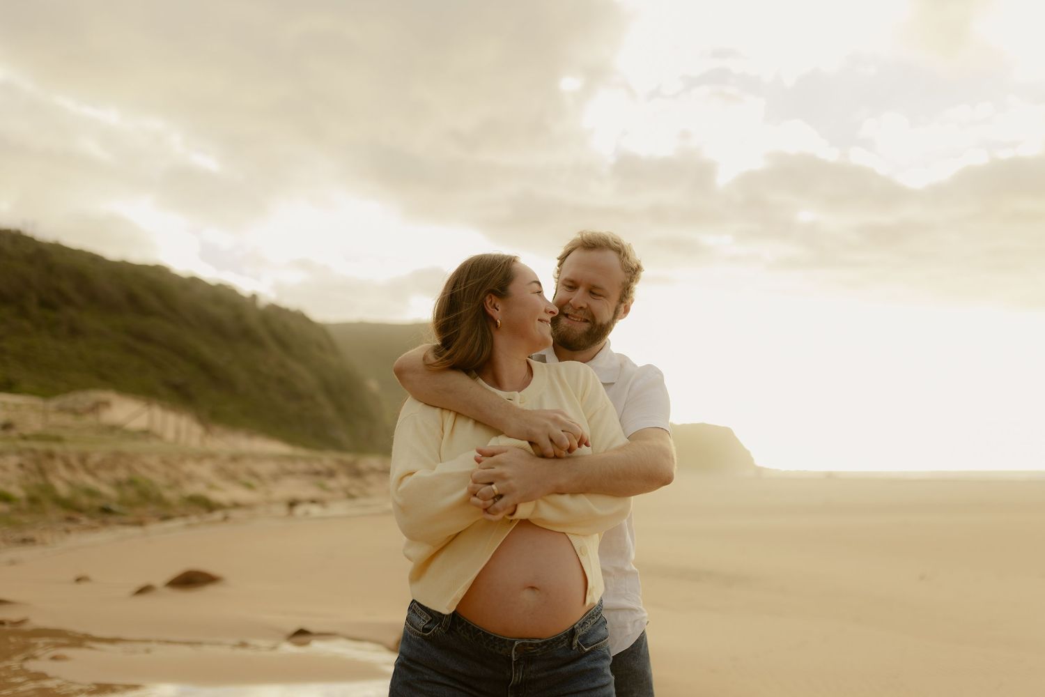 A tender moment between two people embracing on a beach during golden hour.