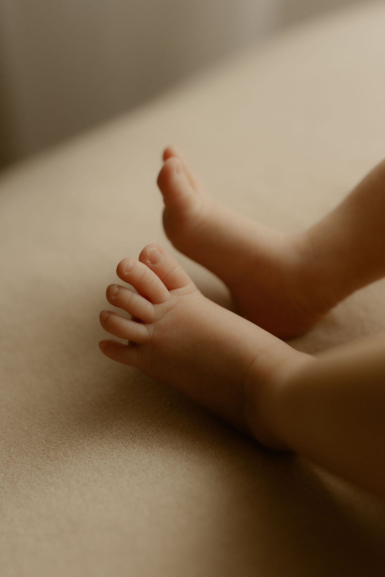 Close-up of tiny newborn baby feet resting on a soft beige surface in warm neutral tones.