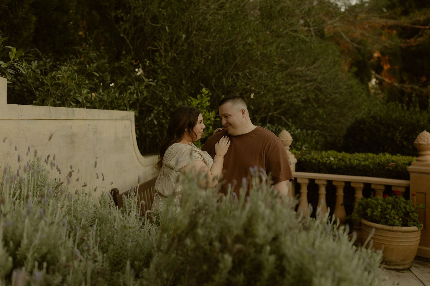 Couple sharing a romantic moment on a garden bench surrounded by lavender and lush greenery at golden hour.