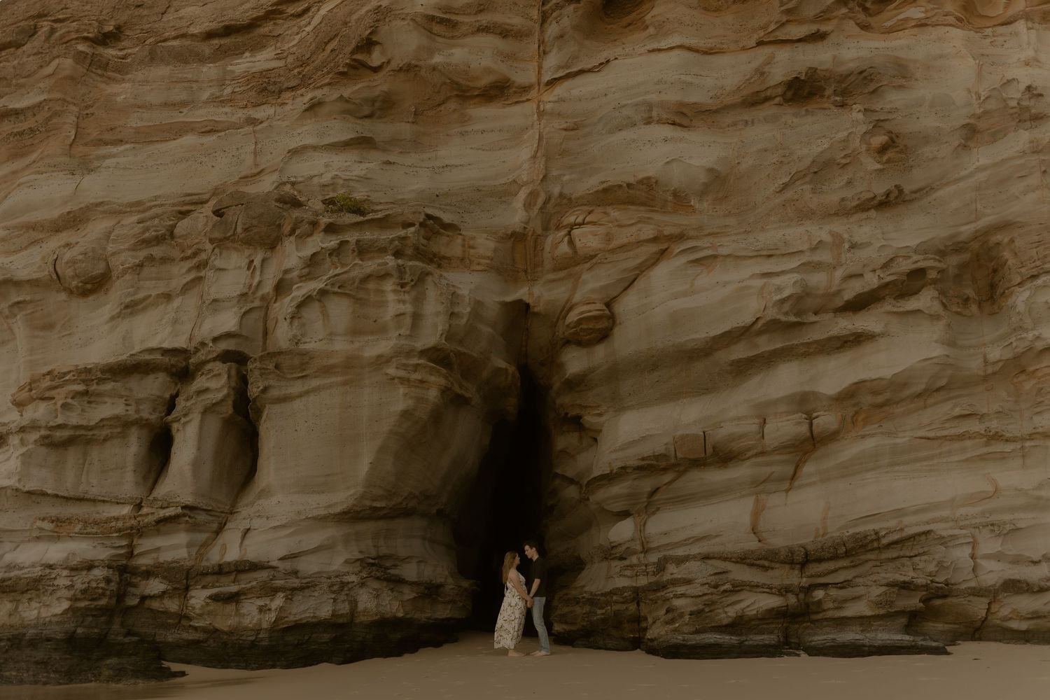 Dramatic coastal cliffs and rock formations along a scenic beach shoreline at sunset.