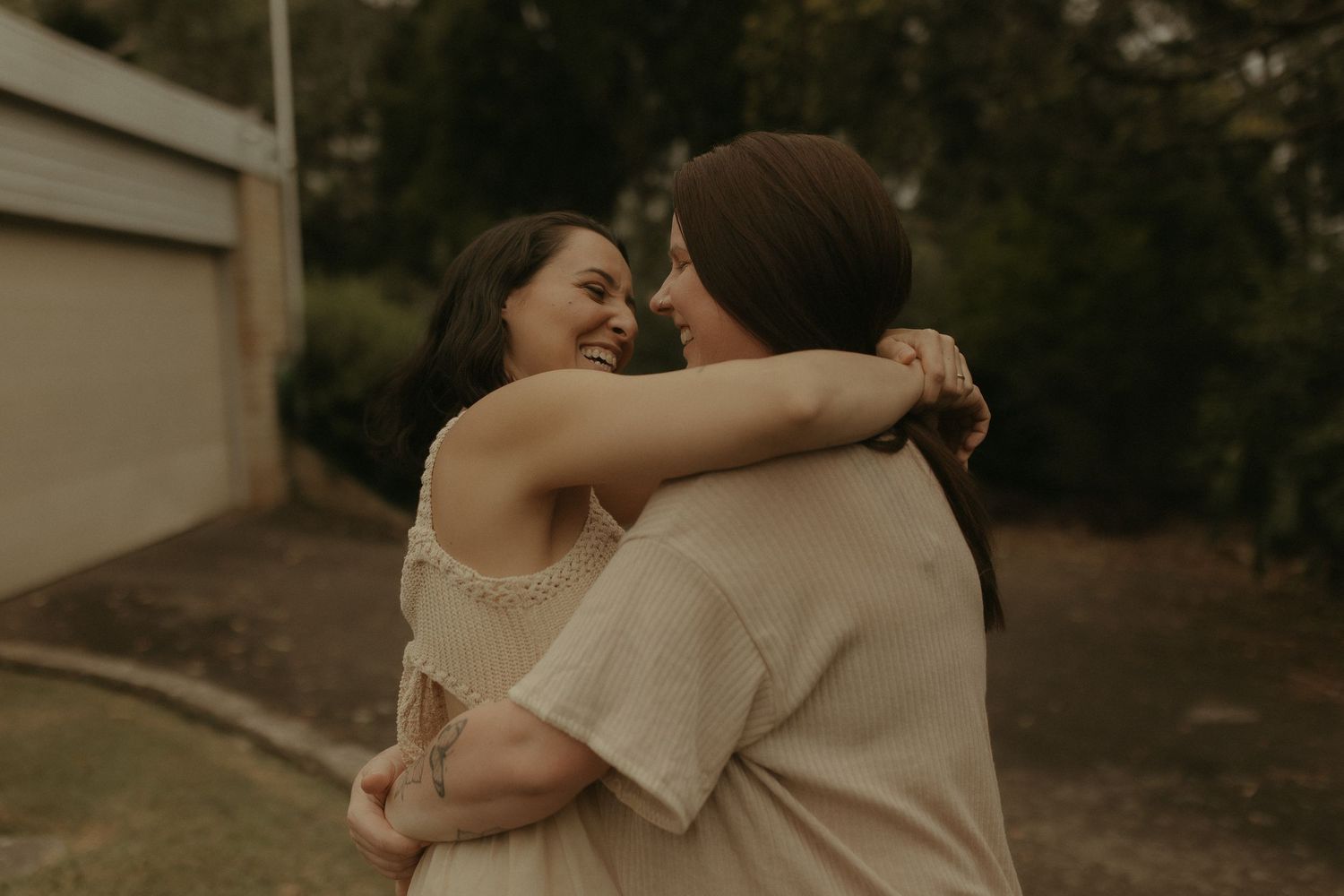 Two people share a warm embrace outdoors in soft, muted lighting against a residential backdrop.
