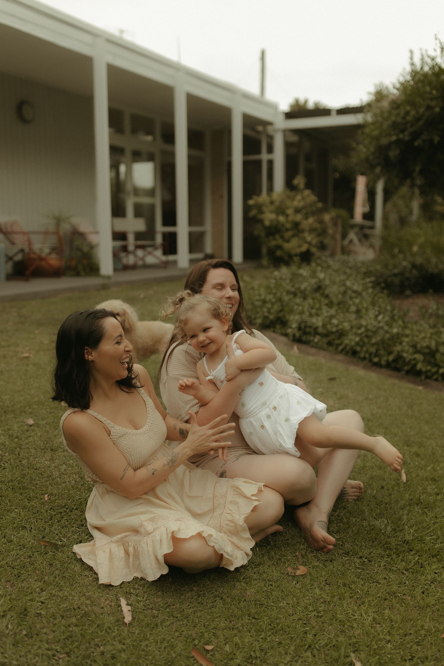 A joyful family moment captured on a lawn in front of a mid-century modern house.