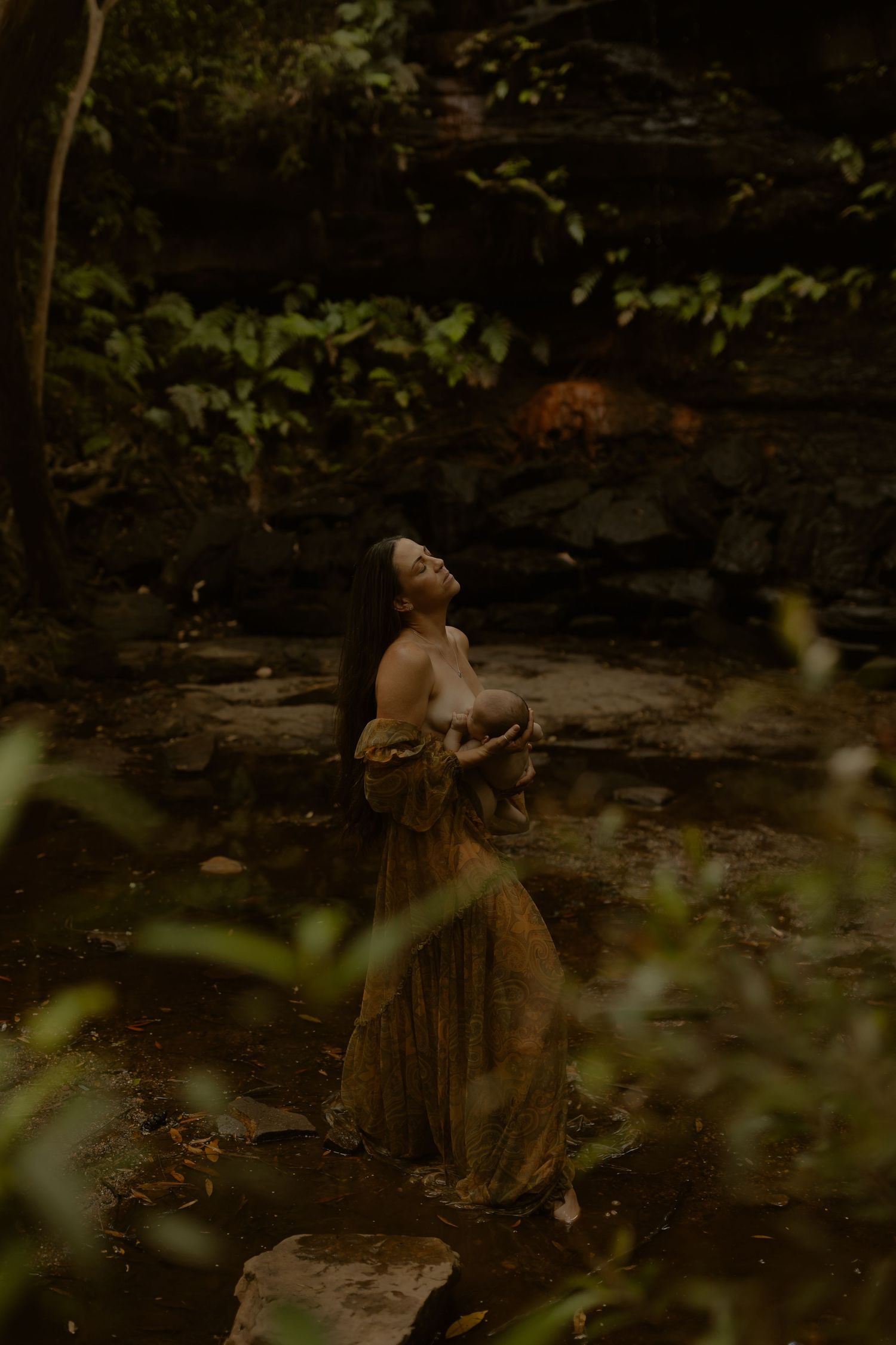 Dreamy portrait of woman in flowing dress standing on rocks in mystical forest setting.