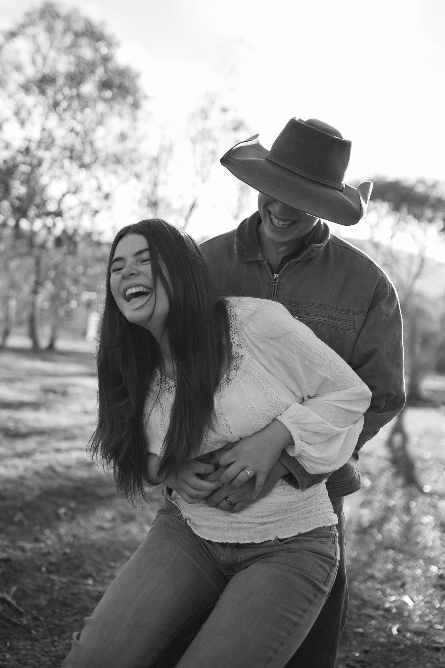 A joyful couple shares a playful candid moment outdoors in black and white photography.