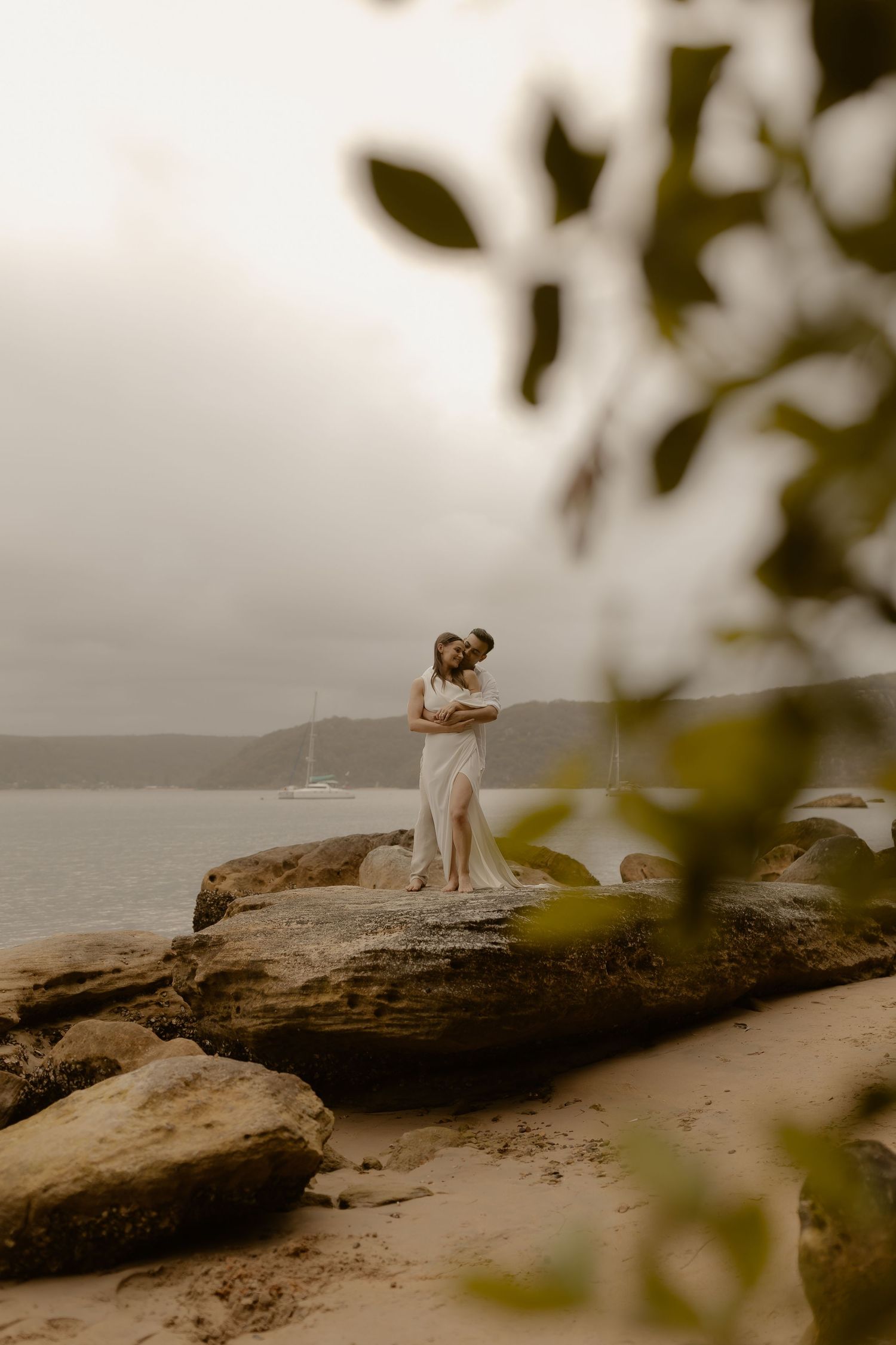 A romantic moment captured on a misty rocky cliff overlooking the ocean with soft natural lighting.