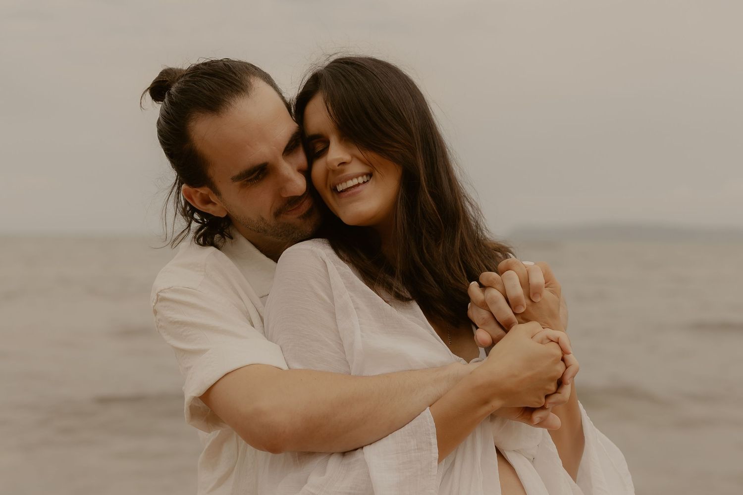 An intimate beach engagement photo capturing a couple embracing at golden hour.