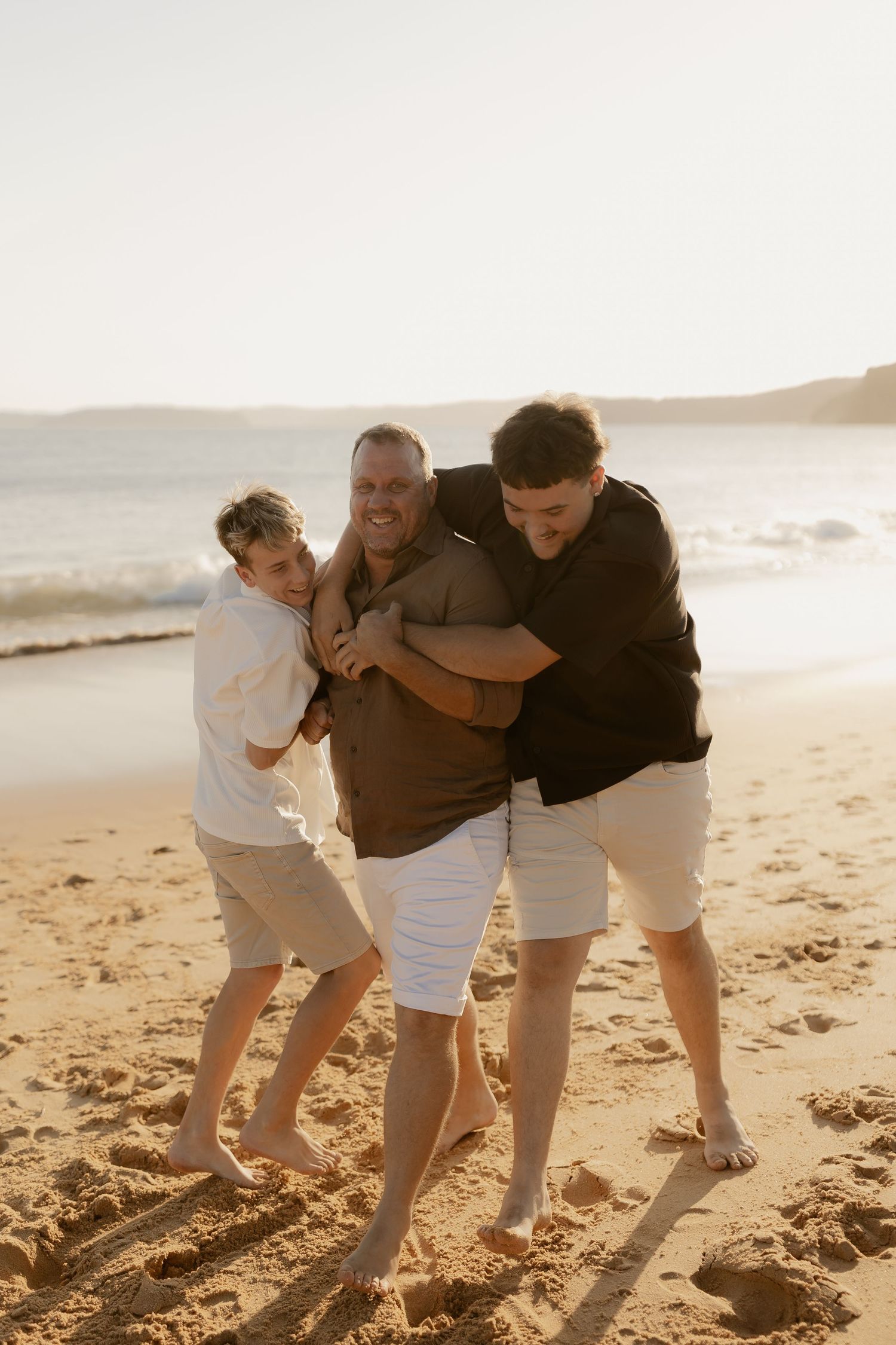 Three figures playfully running along a sandy beach at sunset.