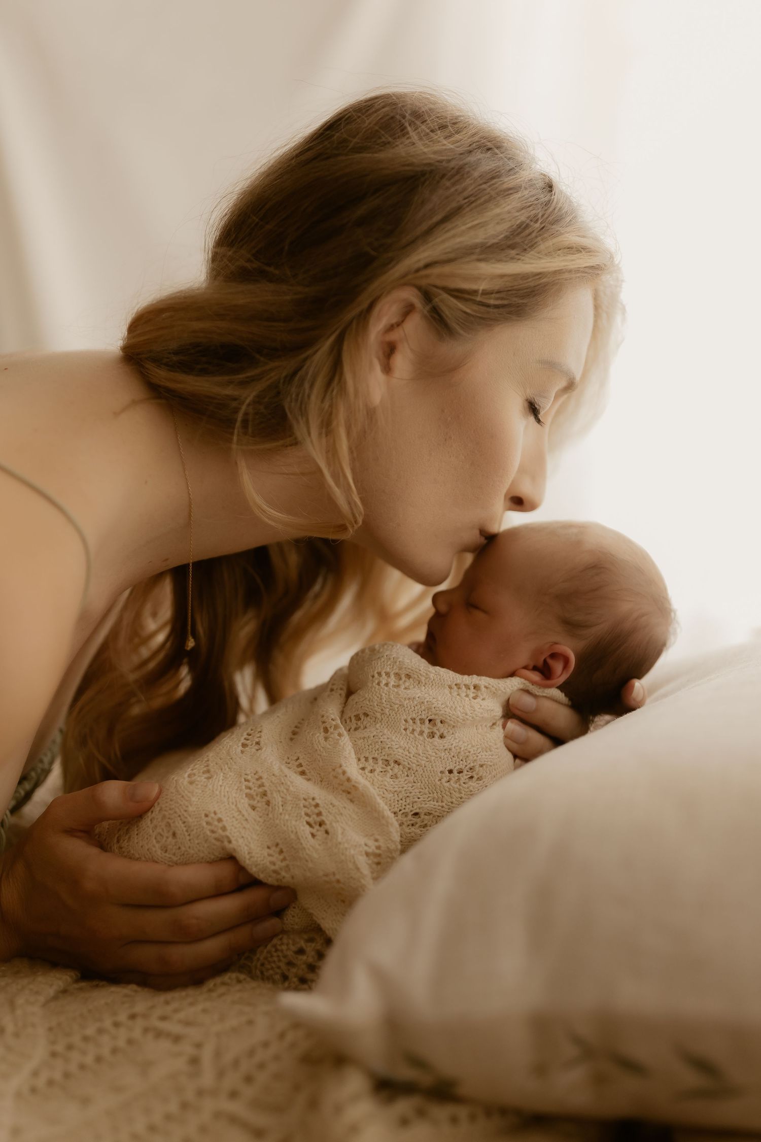 Intimate moment between parent and newborn in soft sepia tones.