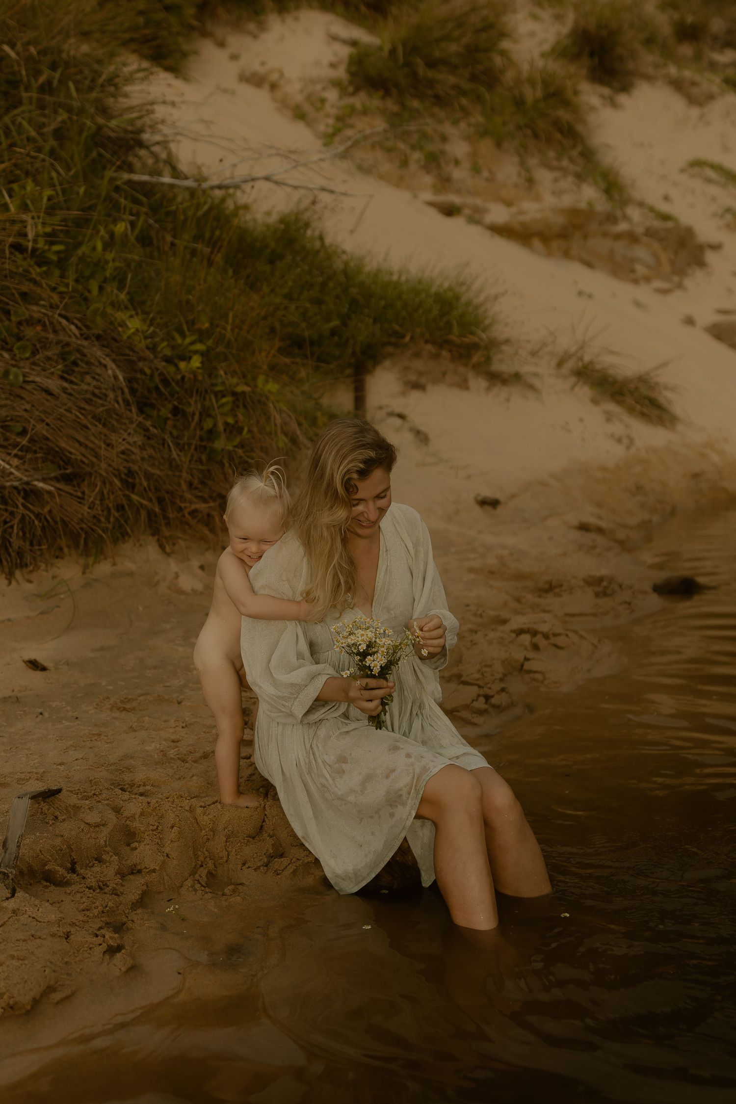 Artistic sepia portrait showing someone sitting on a sandy riverbank in flowing dress.