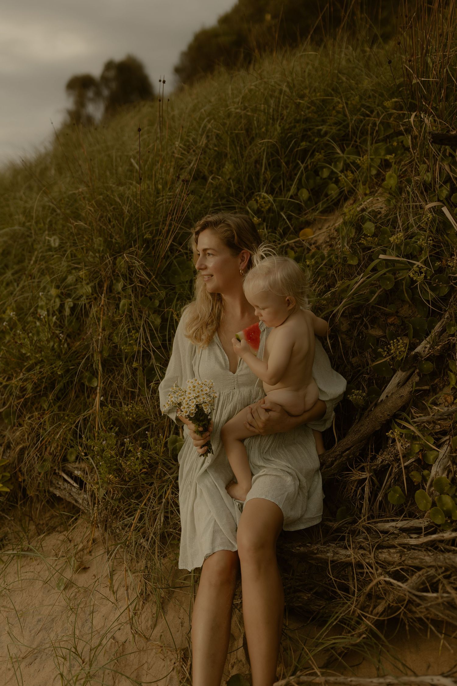A dreamy portrait on a hillside with tall grass and moody overcast sky in muted earth tones.