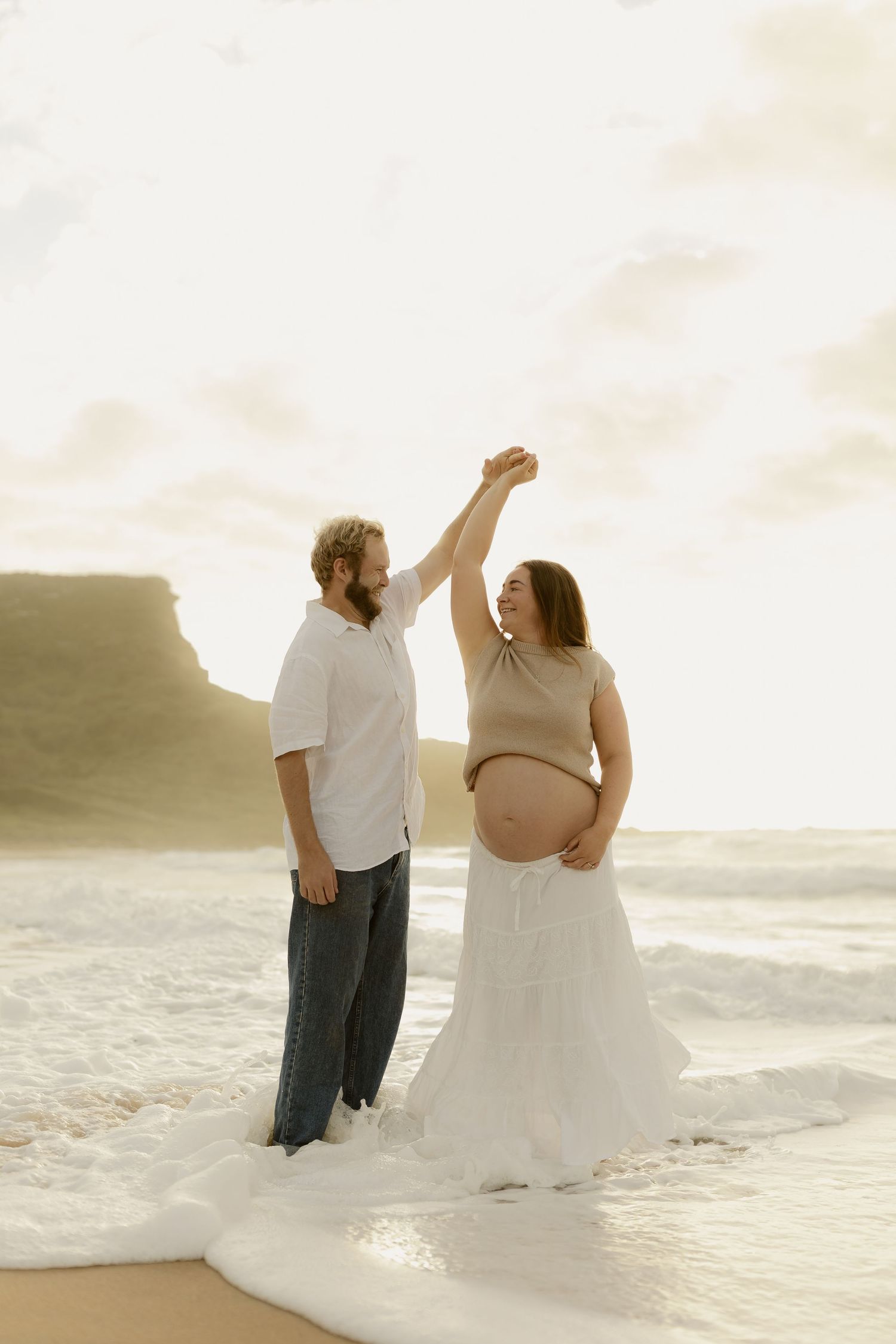 A romantic beach photoshoot with a couple walking along the shoreline at sunset.