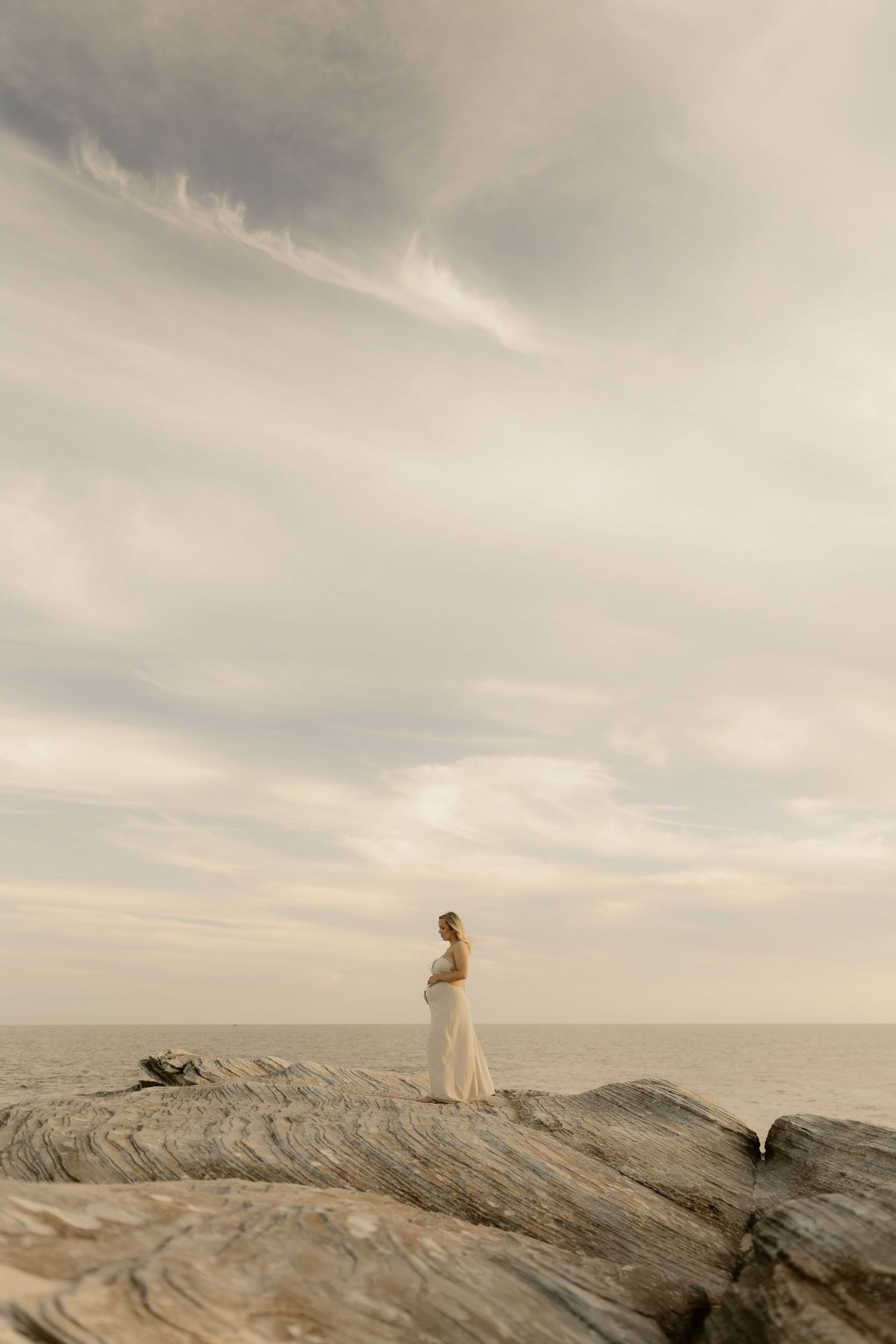 Figures stand on rocky coastal cliffs overlooking a misty ocean horizon at dusk.