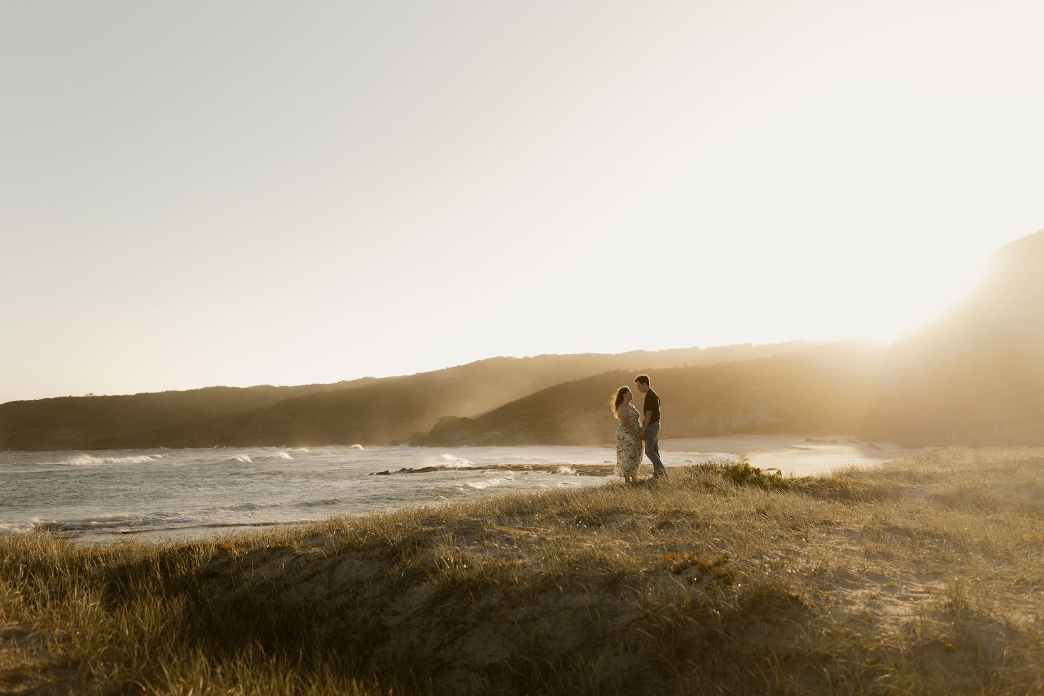 Silhouettes of two people walking along a misty coastal trail at golden hour with dramatic ocean views.