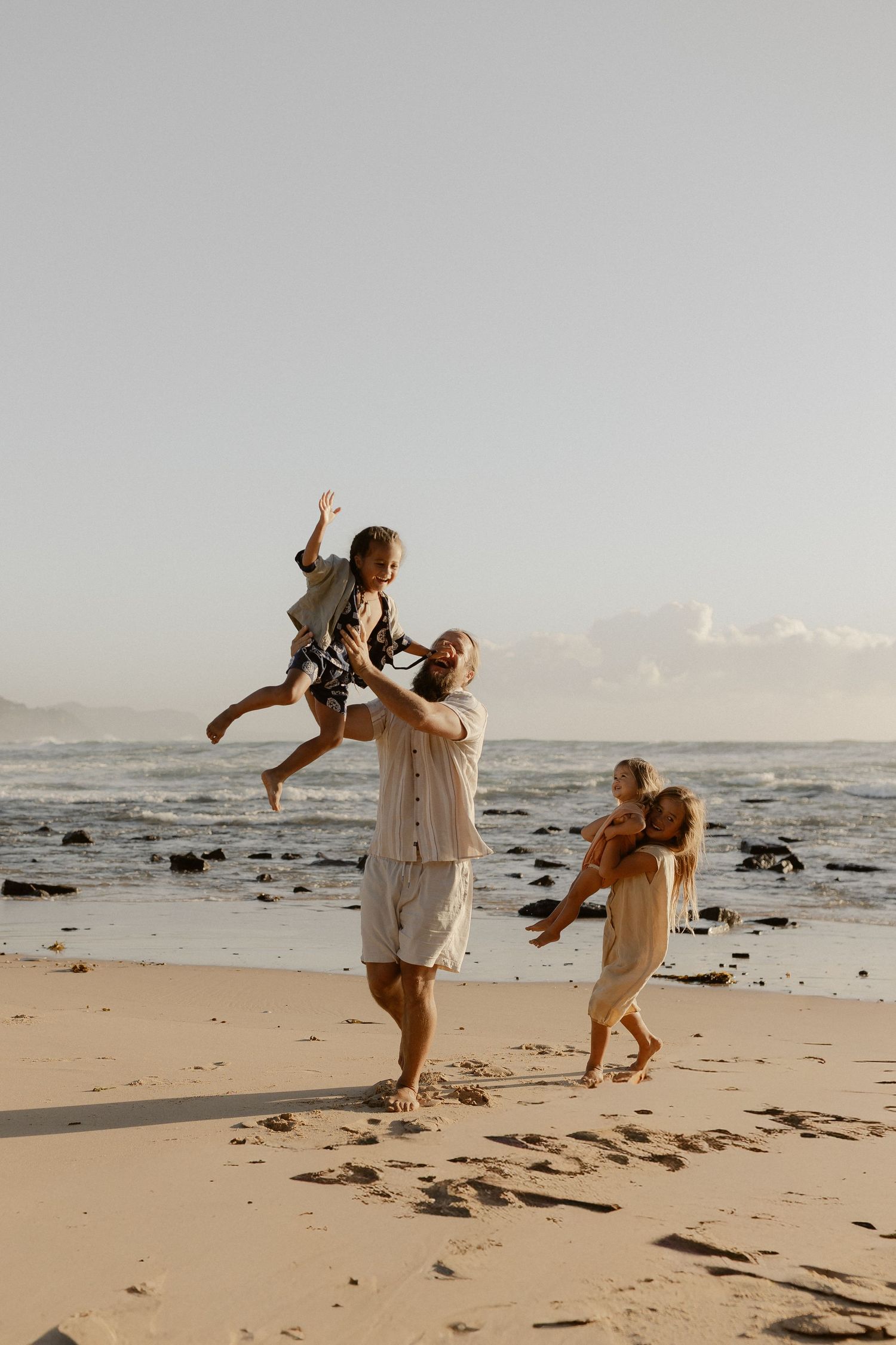 Joyful family playing and lifting children on a scenic beach at sunset.