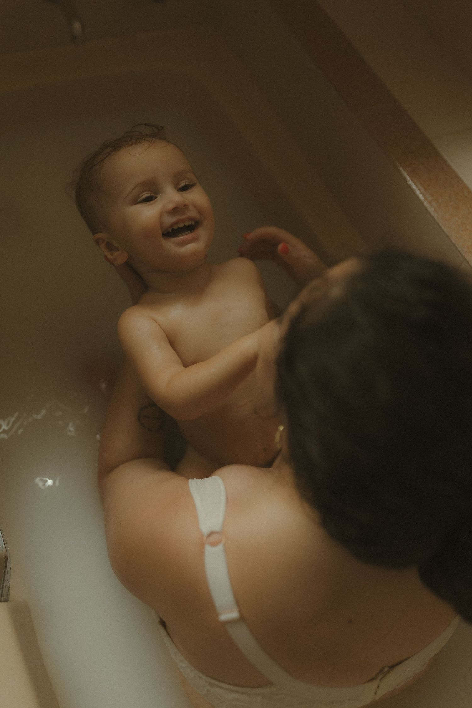 A happy baby laughs and plays during bath time, showing pure joy while splashing in the tub.