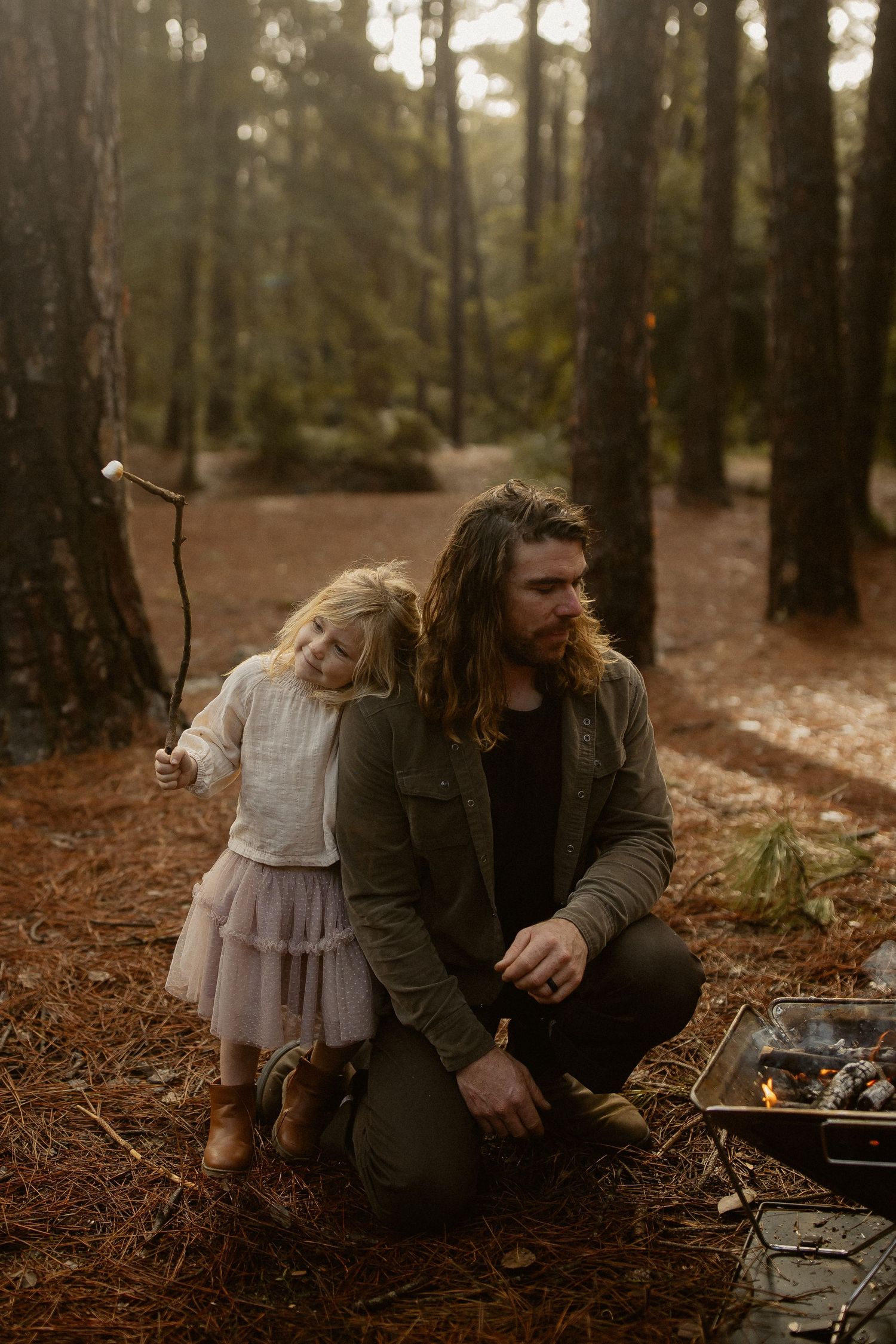 A family enjoys a cozy autumn day around a campfire in a moody forest setting.