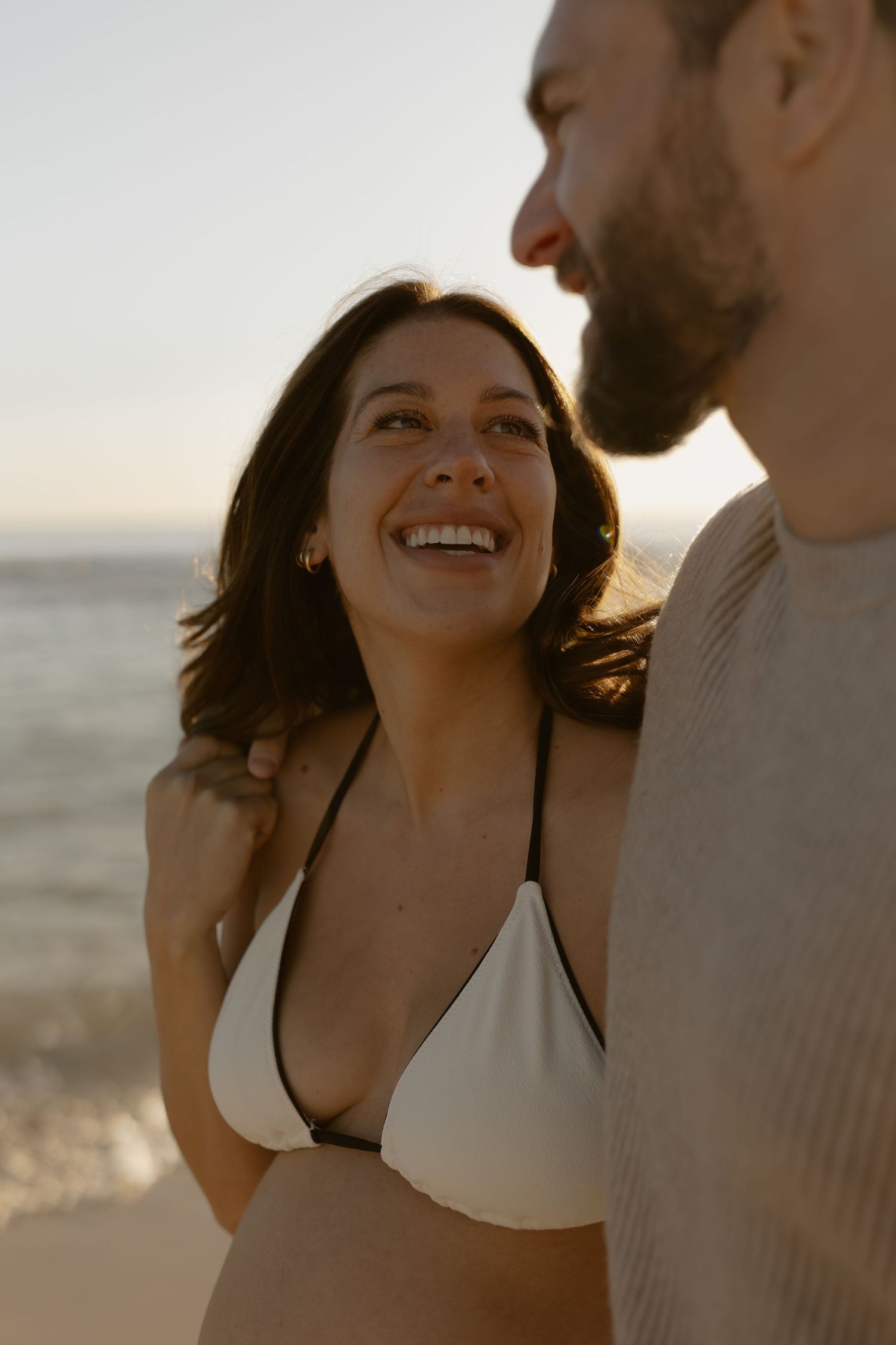 A couple shares joyful laughter during a sunset beach photoshoot.