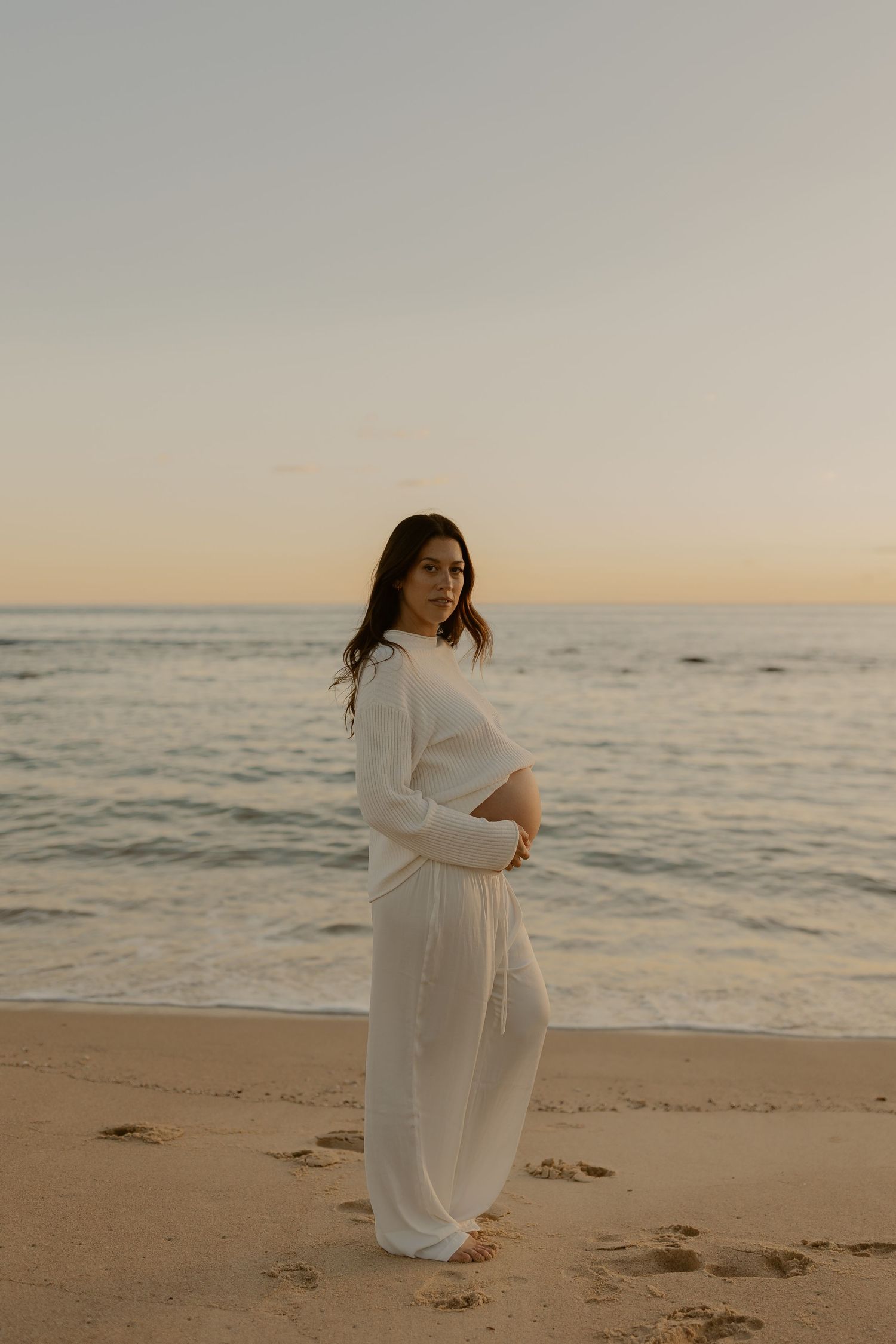 A figure in a flowing white dress dances gracefully along a serene beach at sunset.