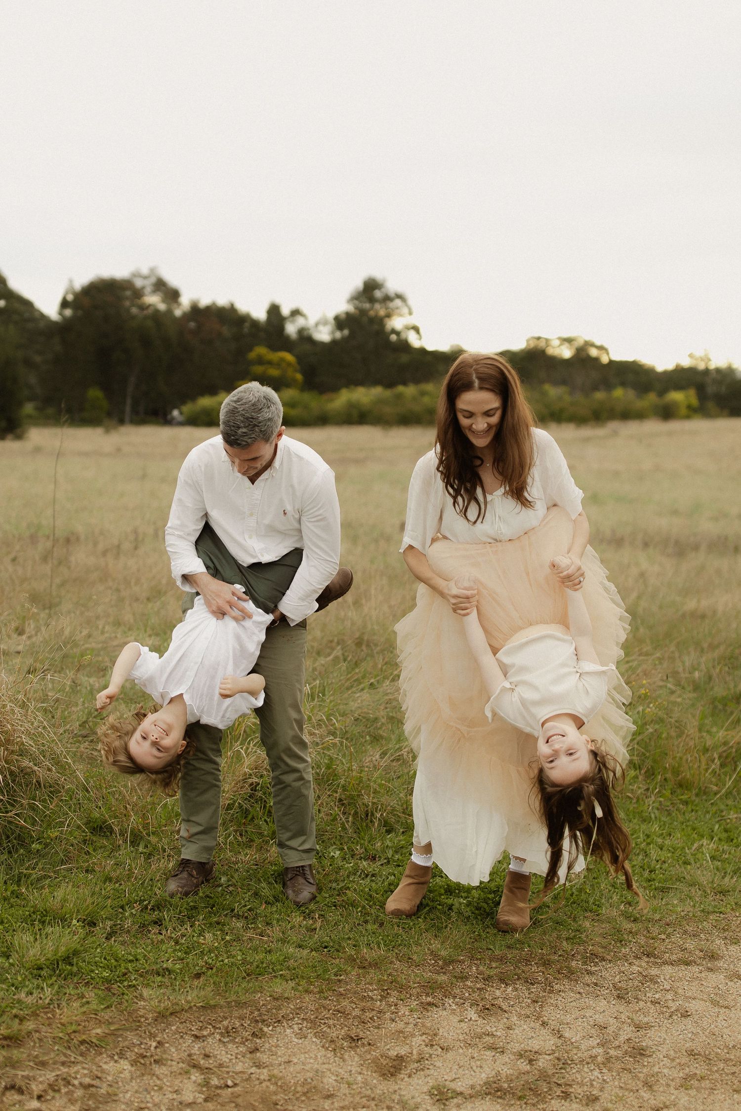 Family playing and laughing together in a rustic outdoor field setting.