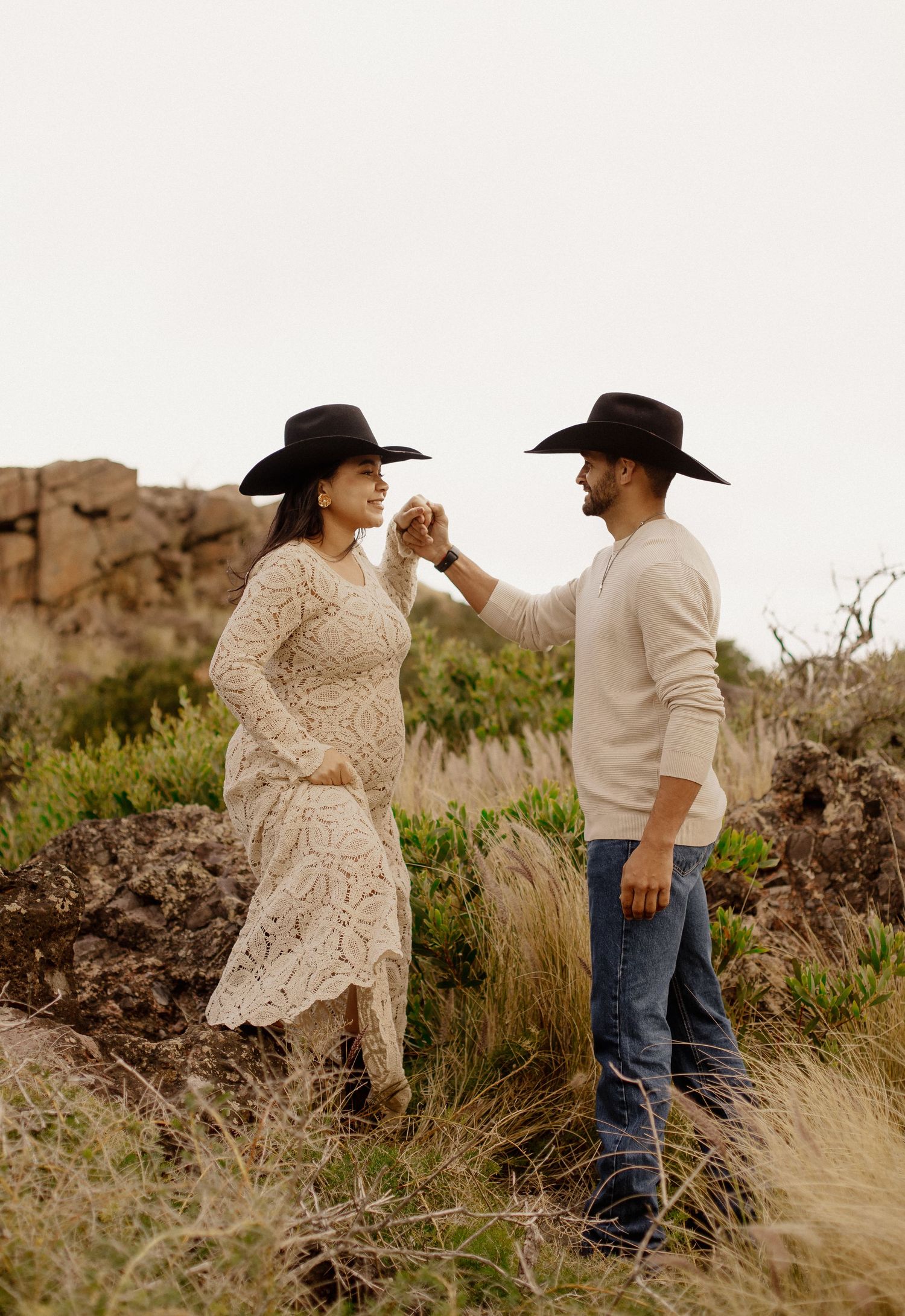A couple in western attire dancing together in a desert landscape during golden hour.