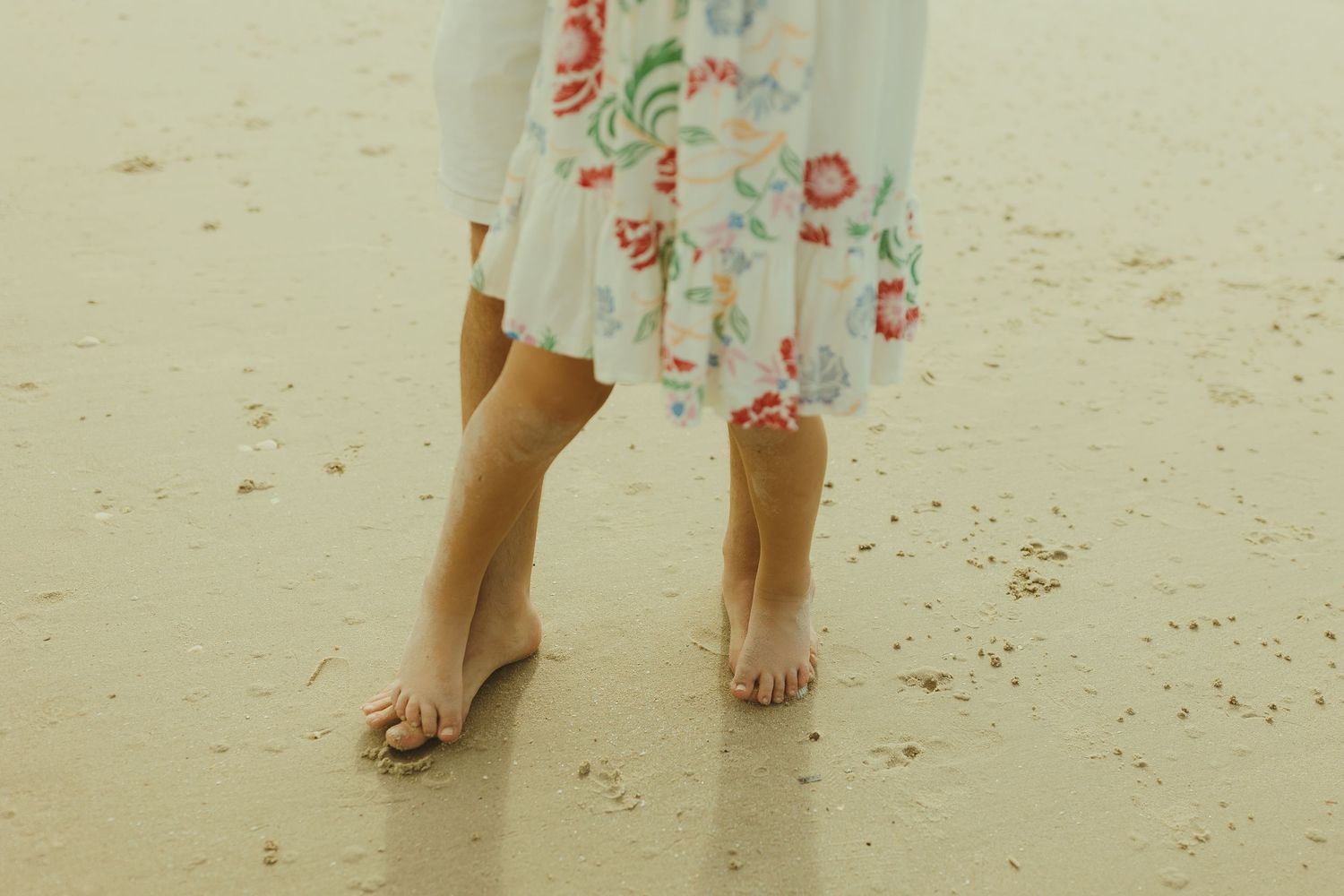 Barefoot person in a floral dress standing on sandy beach.