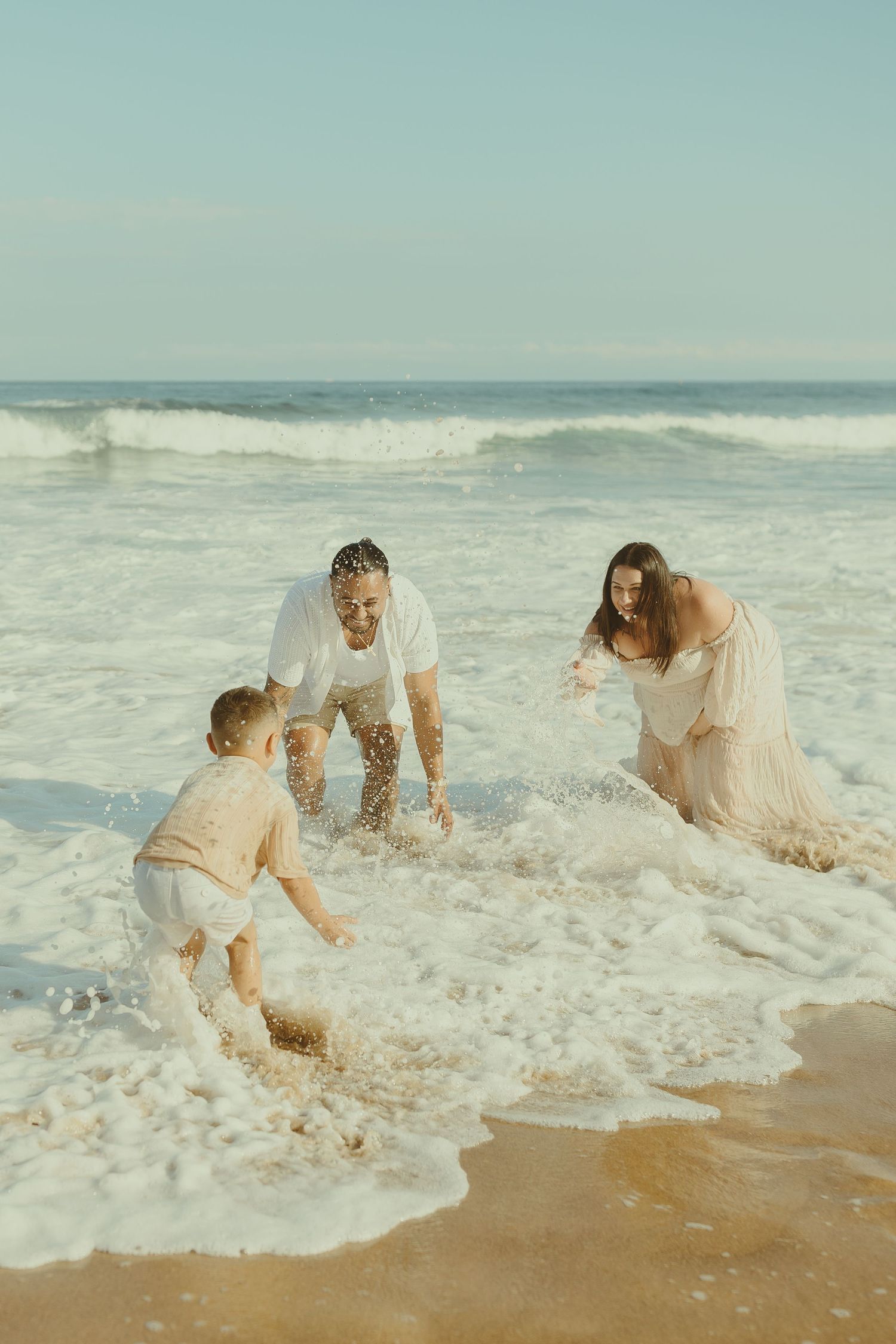 A group plays in the ocean waves on a beach, getting splashed by the incoming surf.