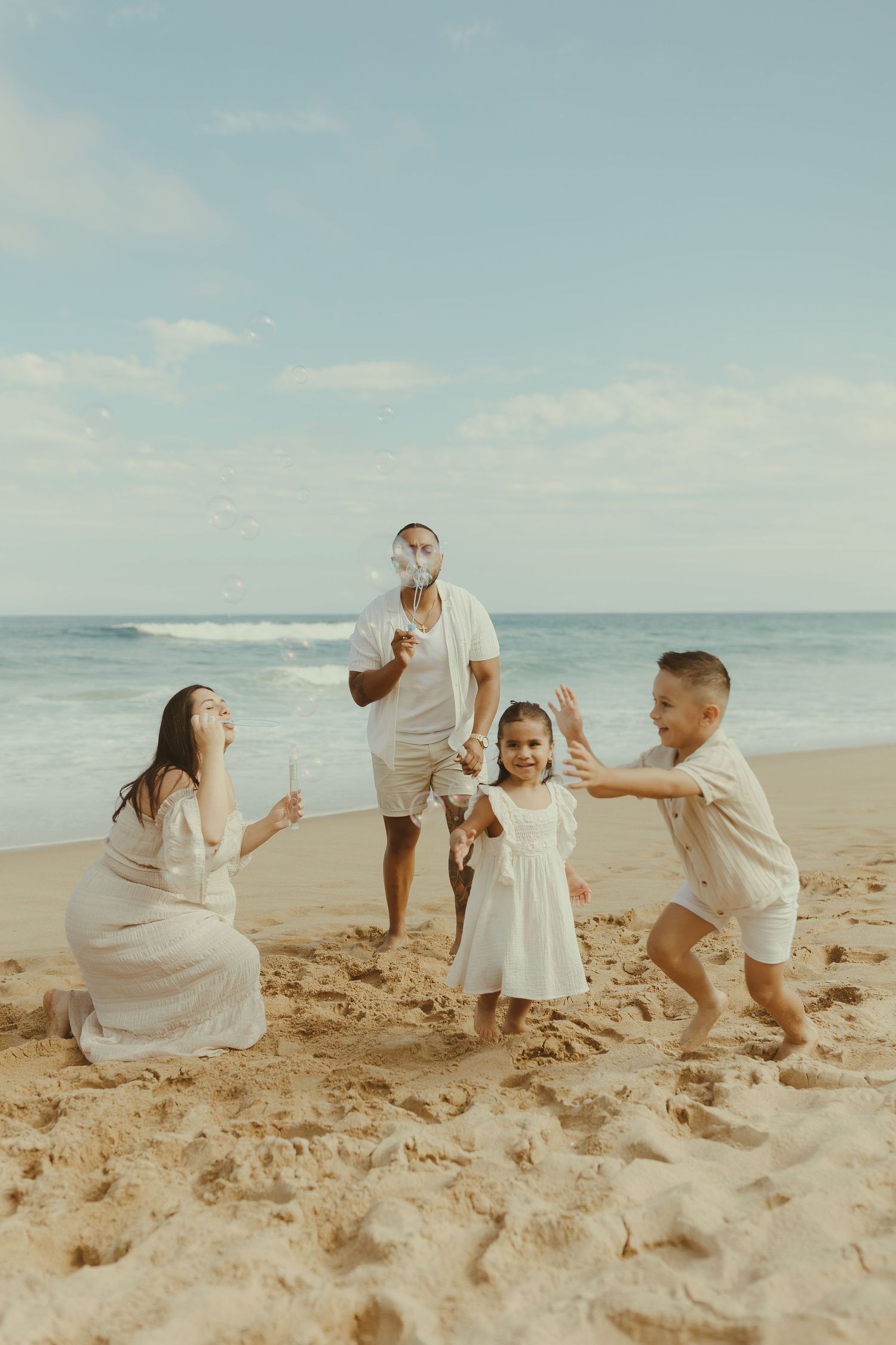 A family in white clothing plays together on a sandy beach, creating a sequence of joyful moments by the ocean.