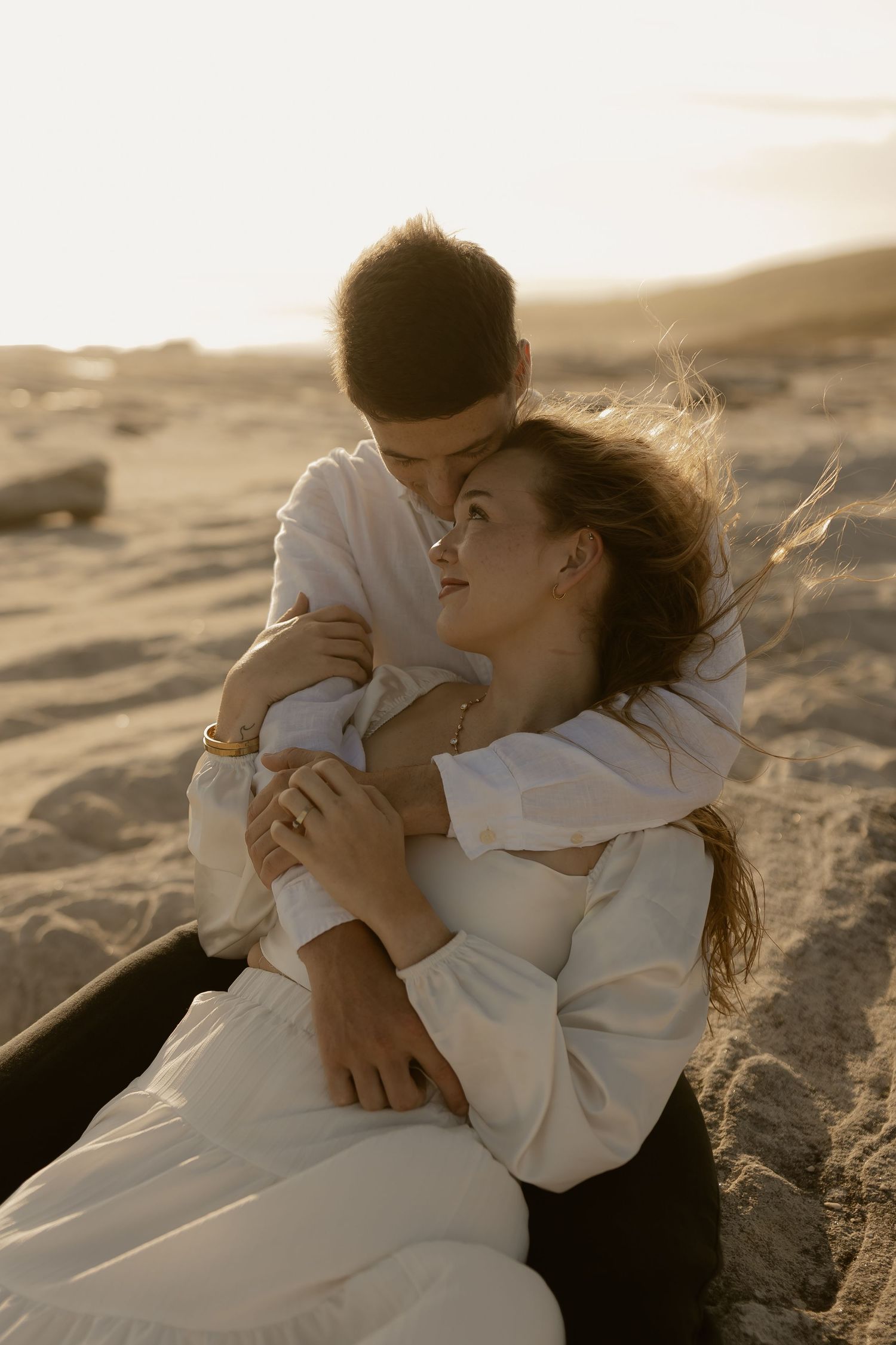 Romantic couple in white clothing sharing intimate moments on beach during sunset.