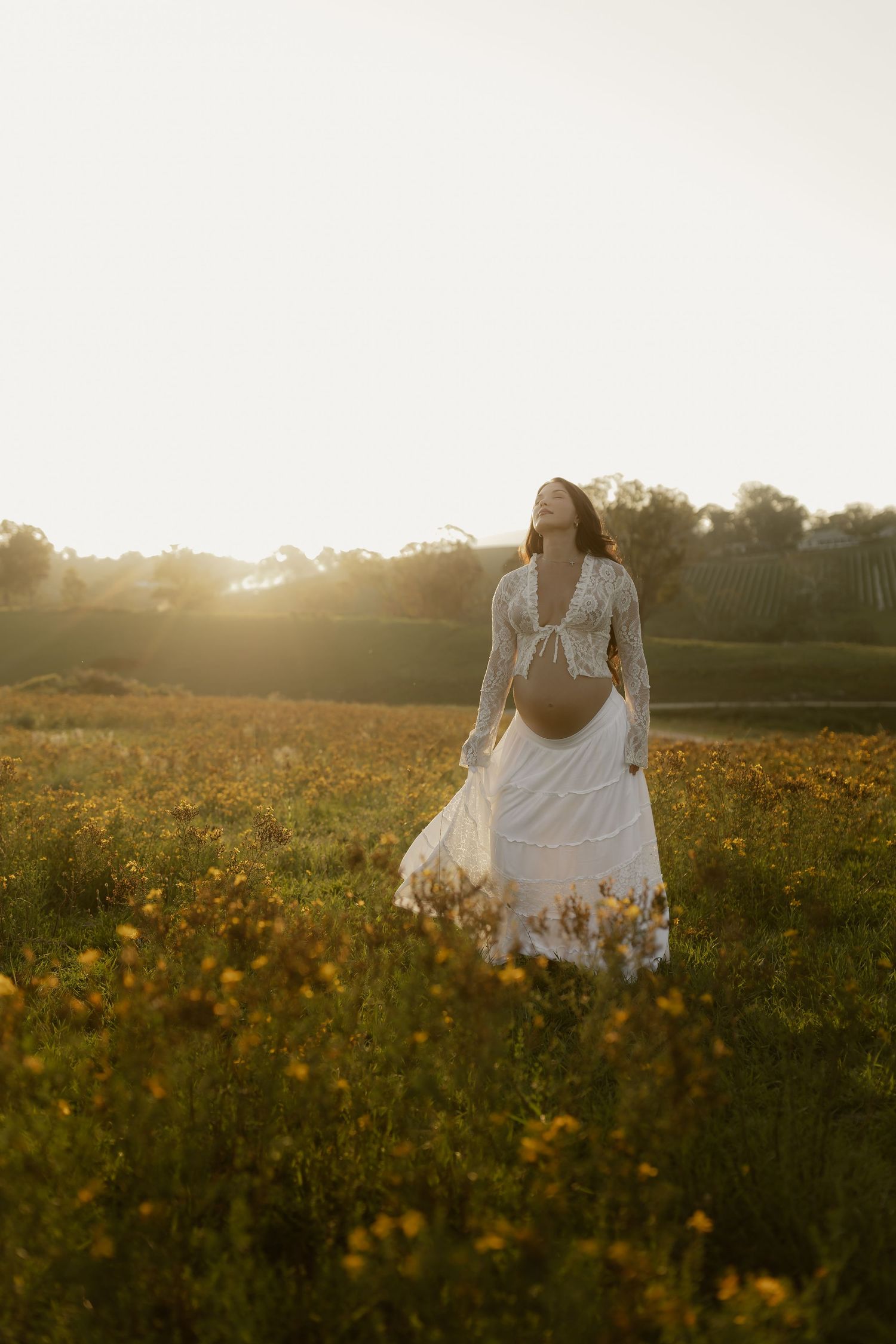 A person in a flowing white dress walks through a golden wildflower meadow at sunset creating a dreamy atmosphere.
