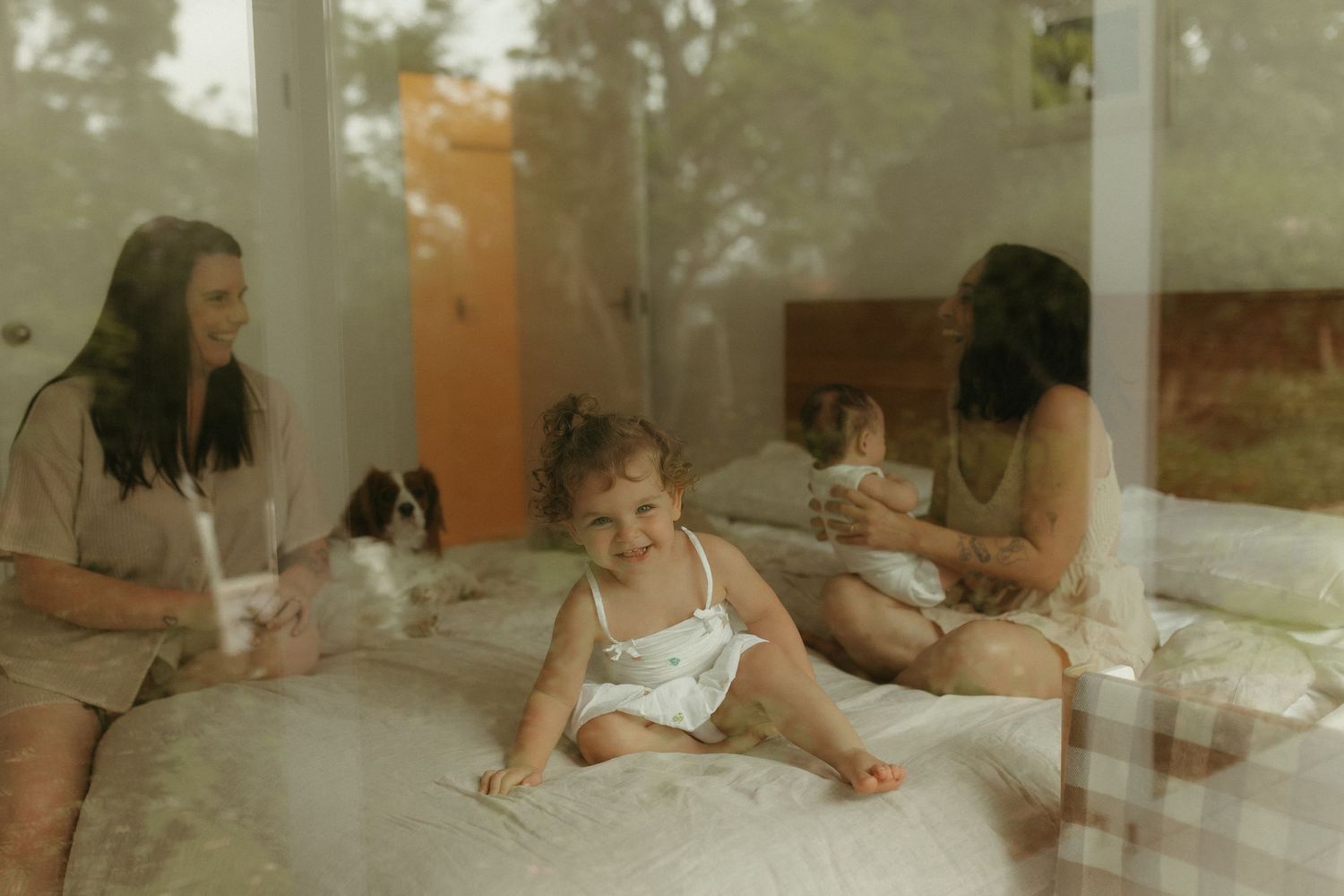 A candid family moment through glass windows showing adults and a baby relaxing in natural light.