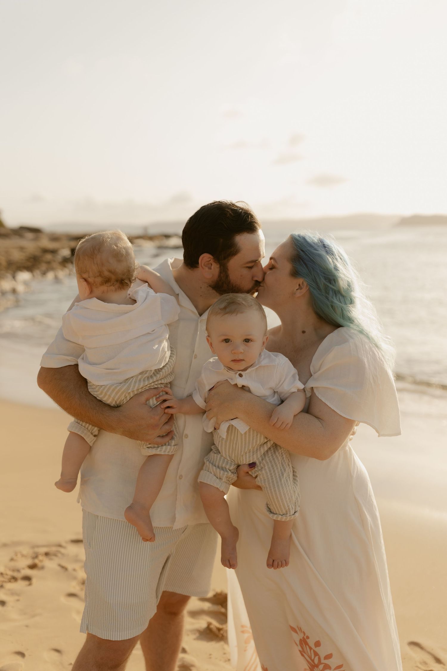 Family sharing tender moments together on a sunlit beach at sunset.
