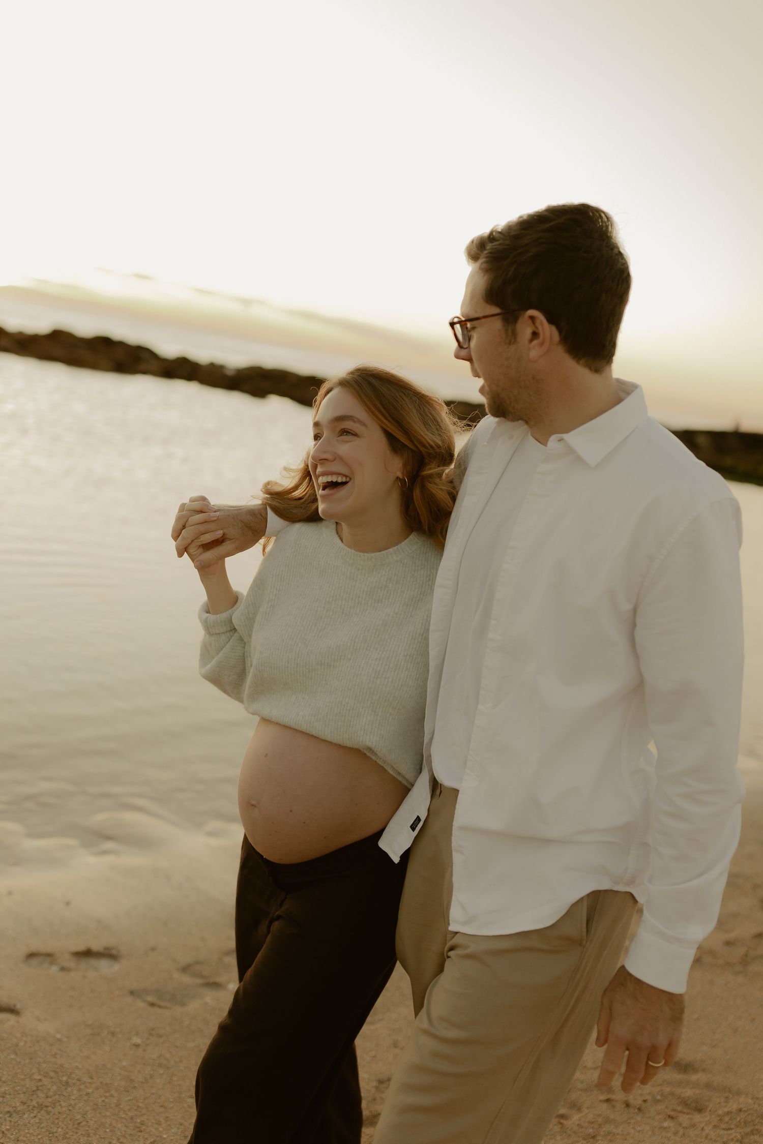 Happy pregnant couple sharing a joyful moment on a sandy beach at golden hour sunset.