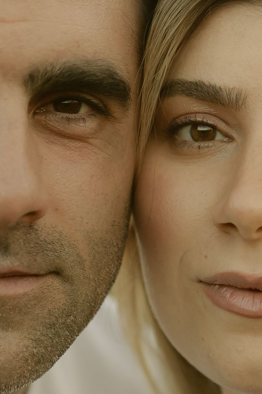 Close-up portrait of a man and woman side by side, showing half their faces with natural makeup and serious expressions.