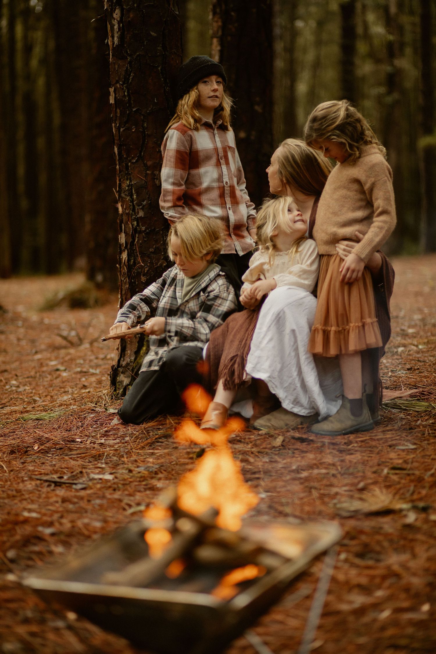 A cozy autumn campfire scene in the forest with people sitting around wearing casual clothing and plaid.