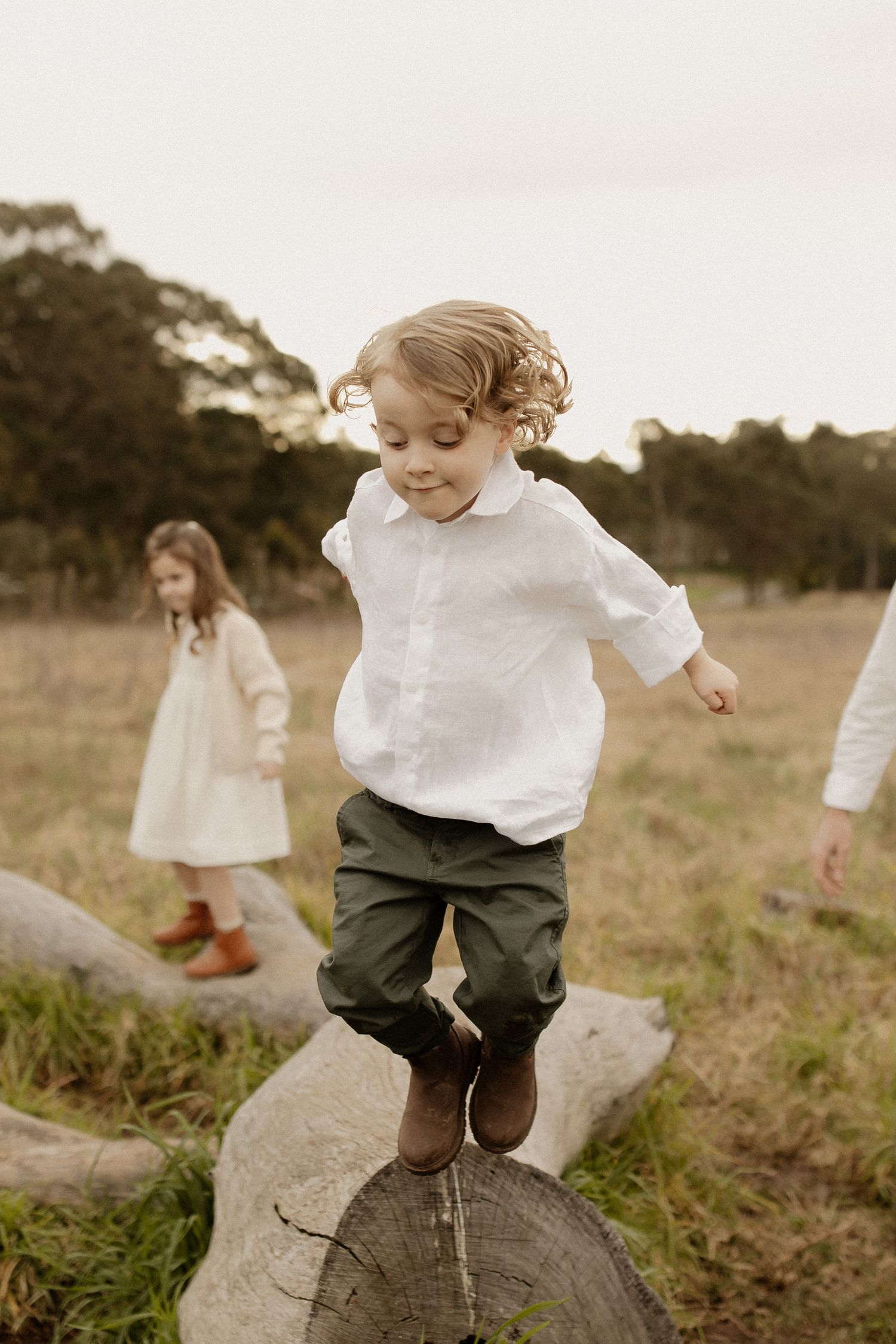 A child in a white shirt and dark pants jumps from a rock in a grassy meadow at sunset.