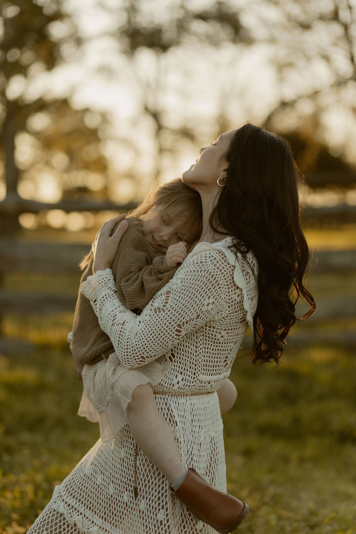 A sweet family moment unfolds in a sunlit field as they share embraces.