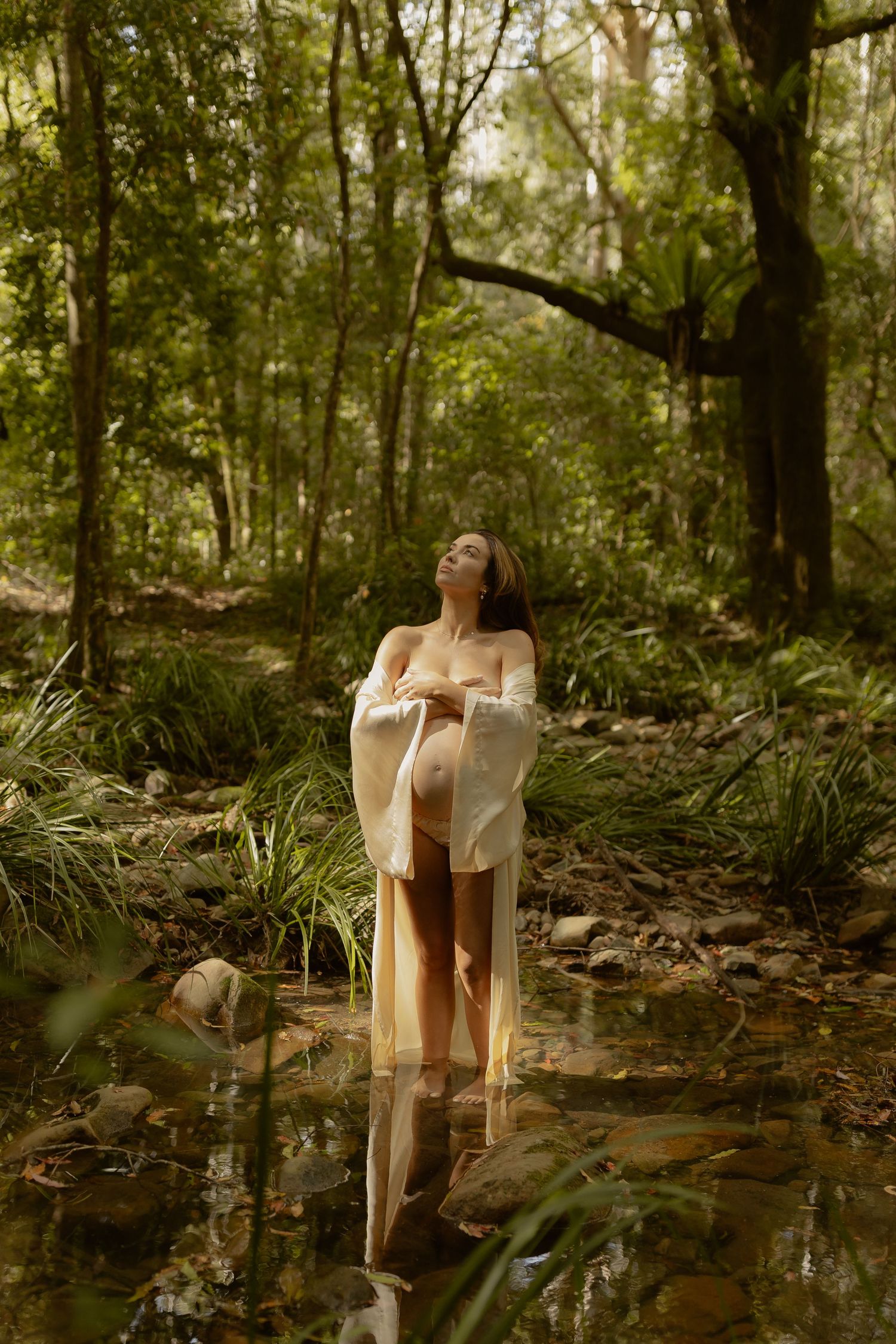 Three ethereal photos show a figure in a flowing white dress standing near a serene forest stream at sunset.