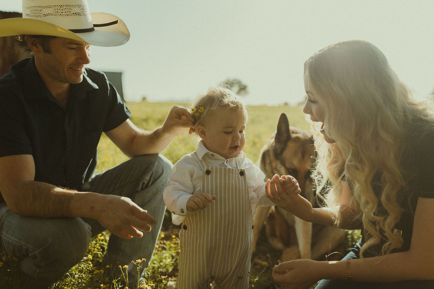 A family shares a tender moment together outdoors during golden hour sunlight in a pastoral setting.