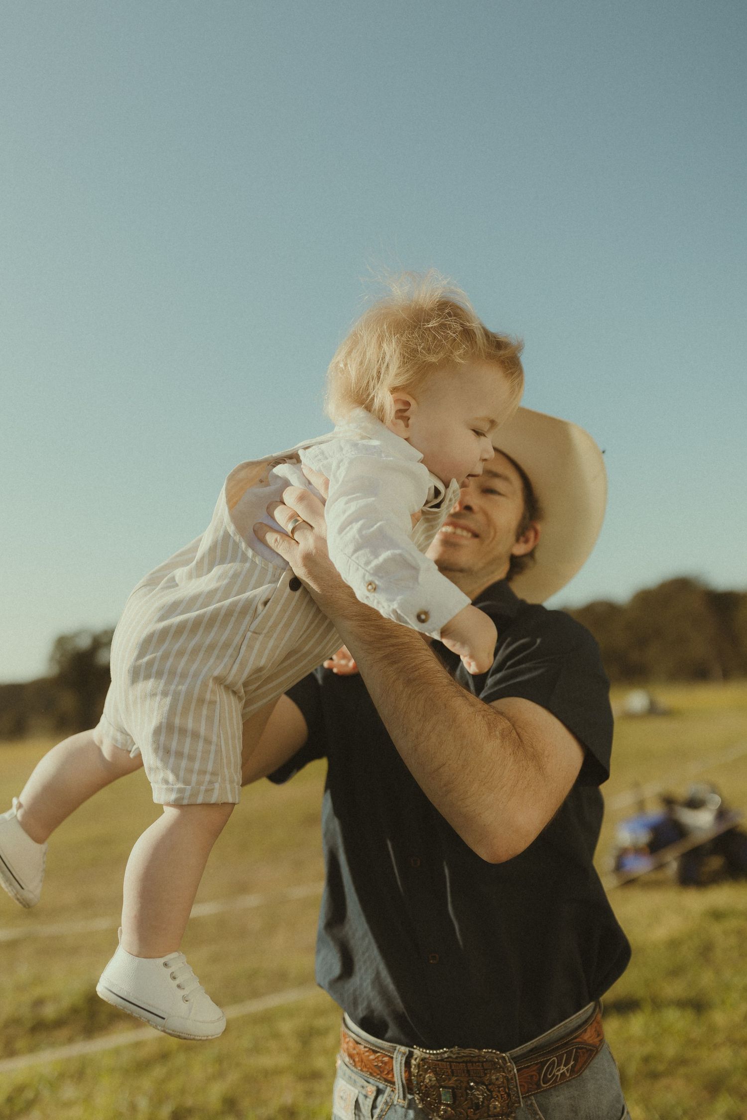 A tender moment captured outdoors in a field on a bright sunny afternoon.