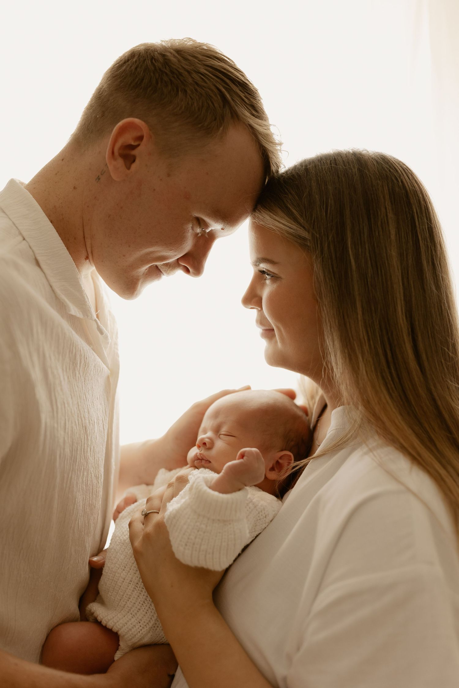 Warm family portrait showing intimate moment with sleeping newborn between parents.
